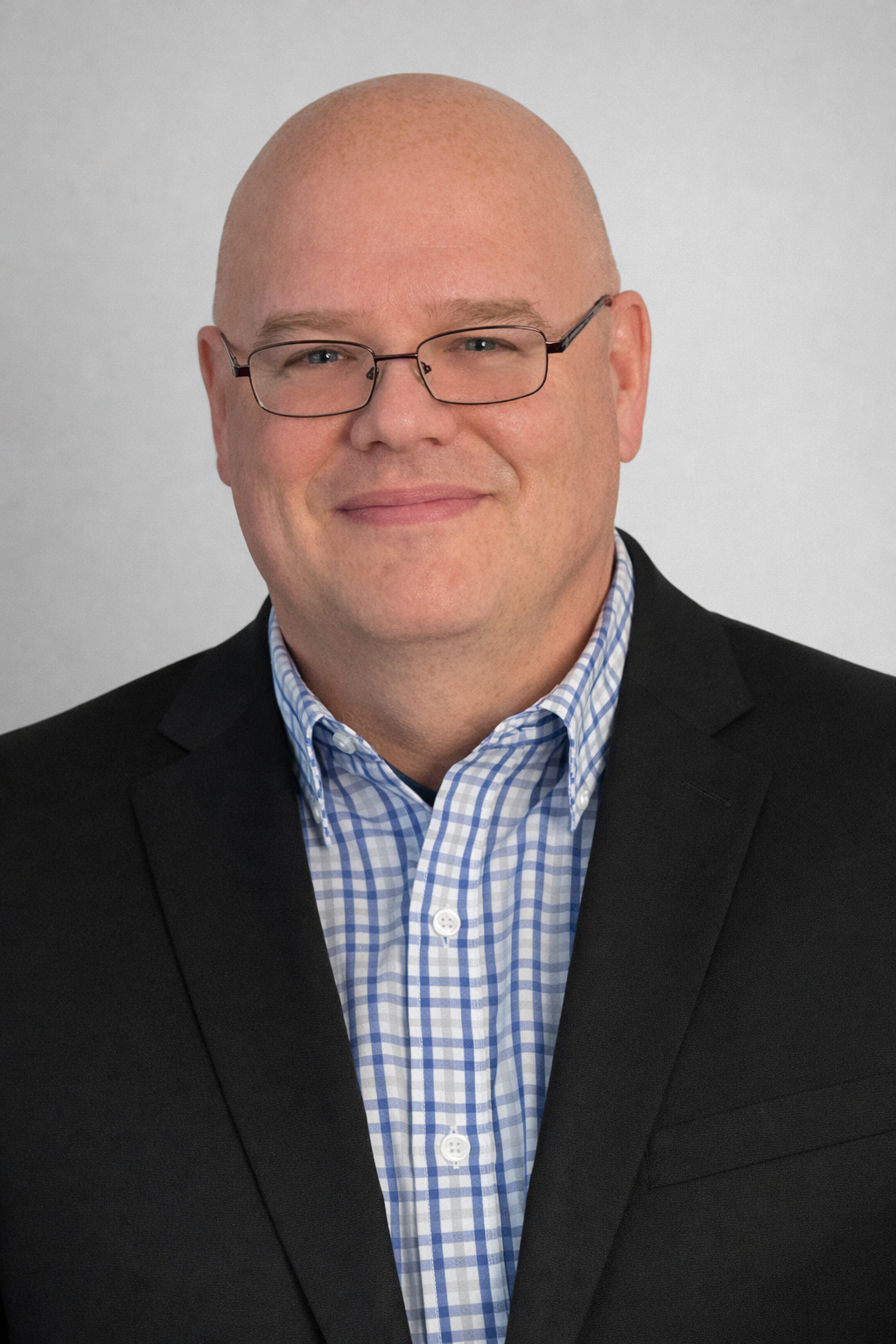 Professional portrait of author John Anno wearing glasses, a black blazer, and a blue‑and‑white checkered shirt against a light gray background.