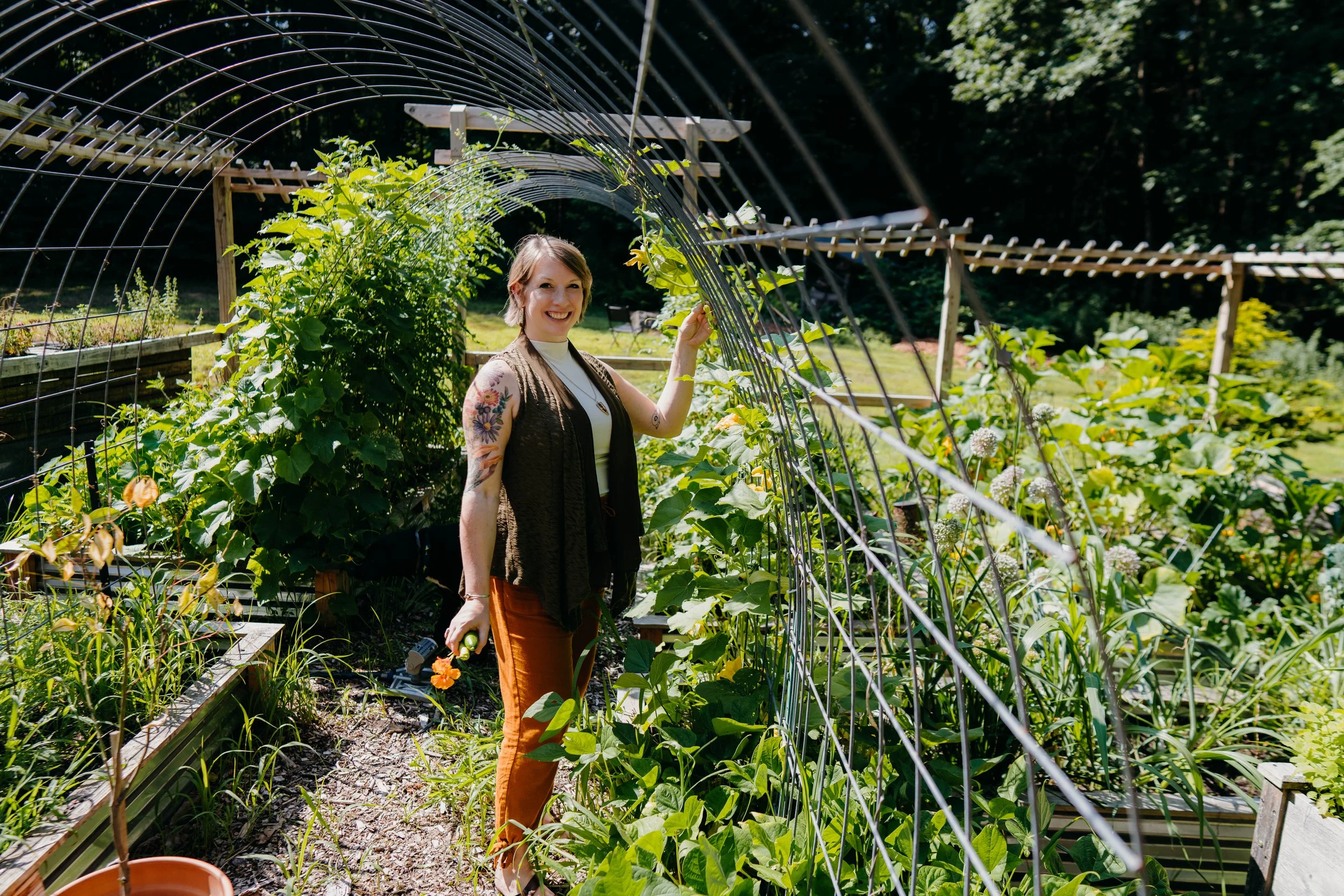 Beth standing under a garden archway covered in foliage.