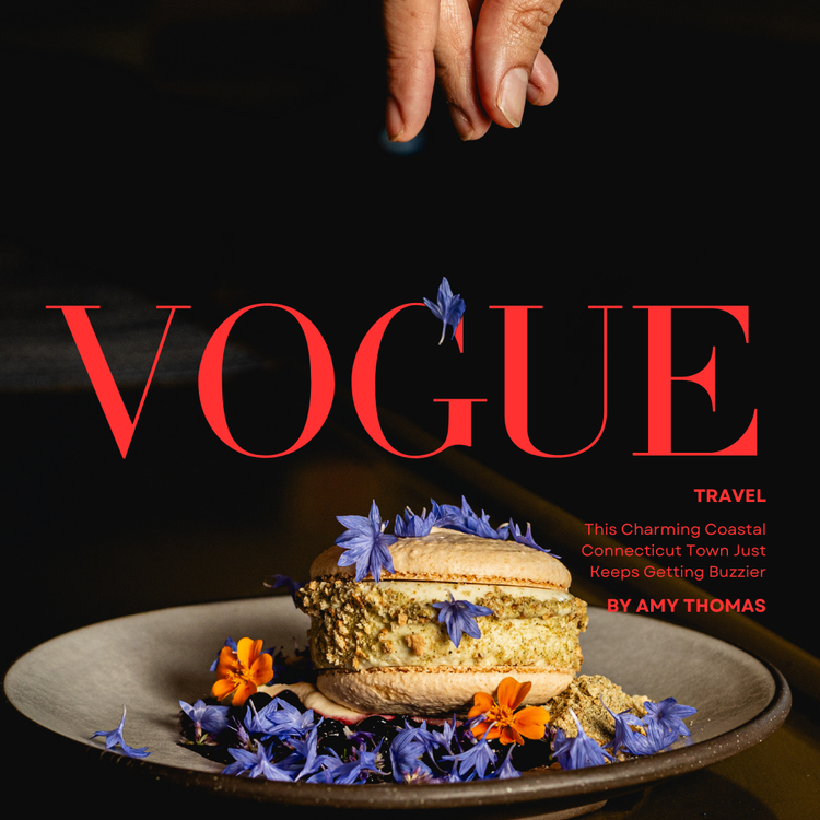 Vogue magazine cover featuring a layered cake with purple and orange edible flowers on a dark plate, and a hand sprinkling a blue flower on top, set against a dark background.