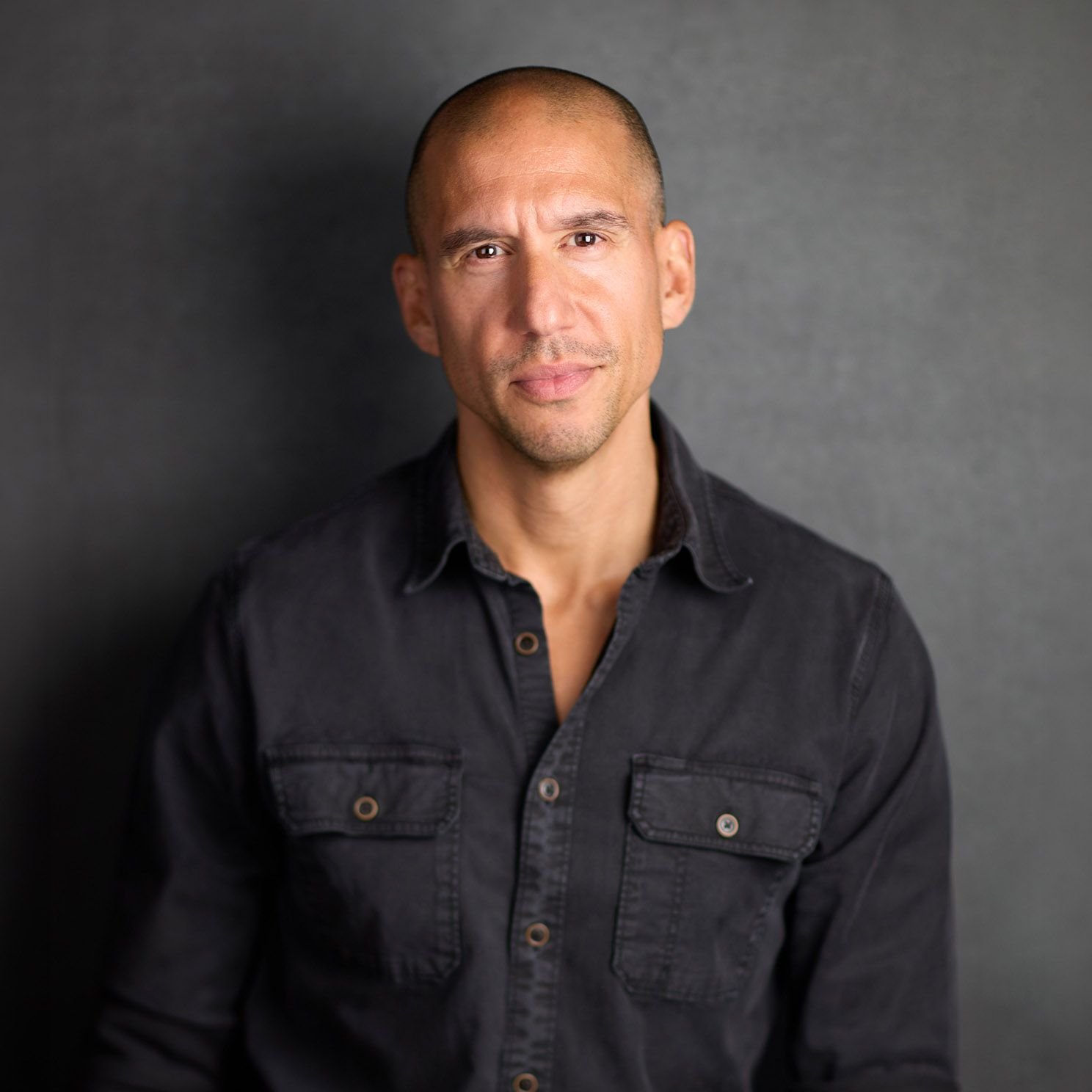 Portrait of Michael Cinquino, a man with a shaved head, wearing a dark button down shirt, looking at the camera.