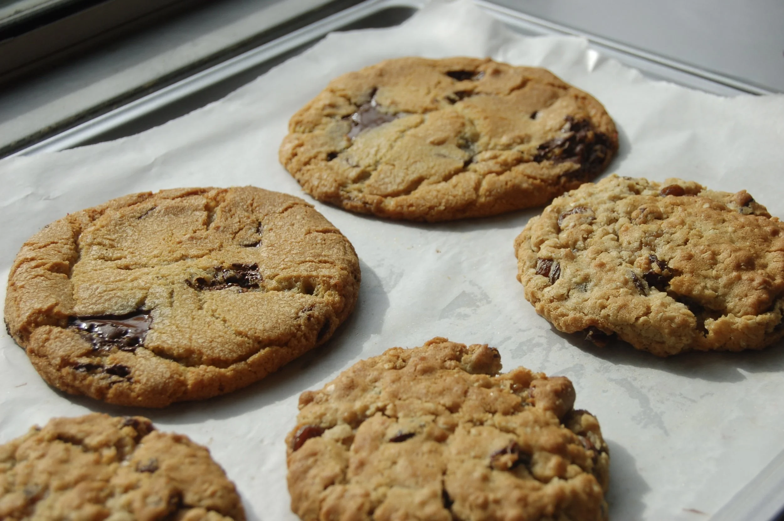 Several chocolate chip cookies on parchment paper placed on a metal baking sheet.