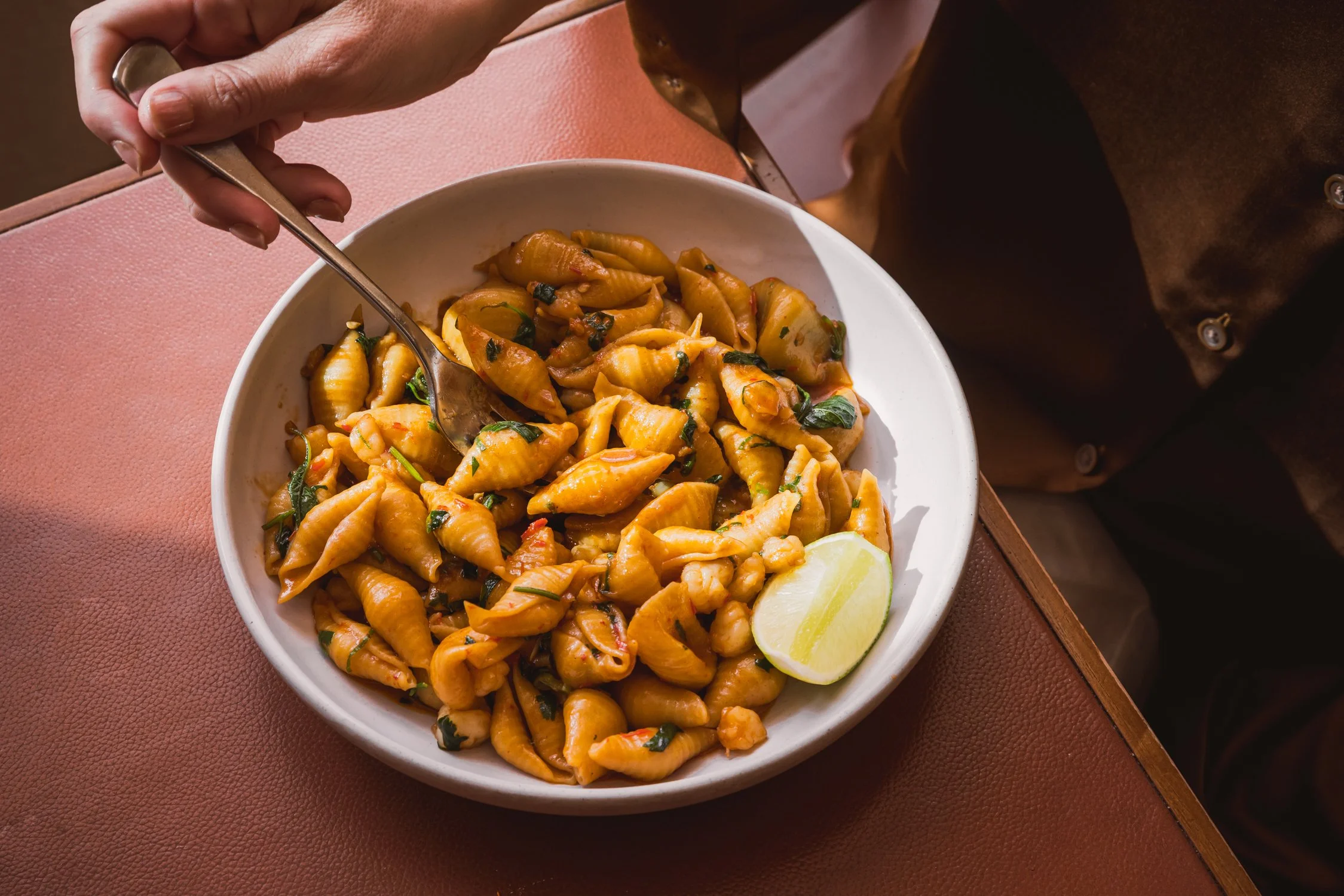 A bowl of cooked pasta with sauce, garnished with chopped herbs, with a lemon wedge on the side.