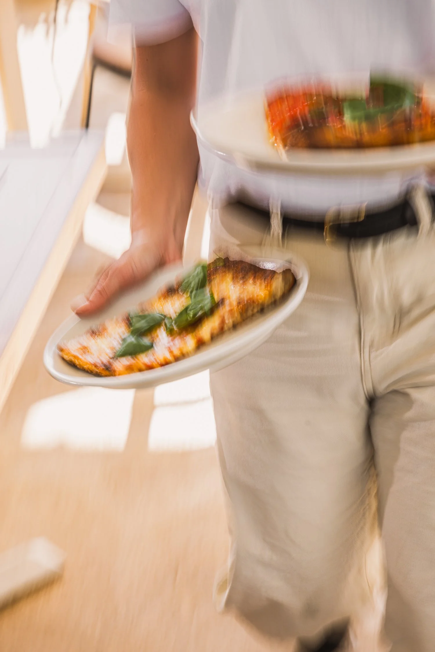 A person is serving a plate of grilled fish garnished with basil leaves, with a bowl of colorful stew or sauce on a serving stand nearby.