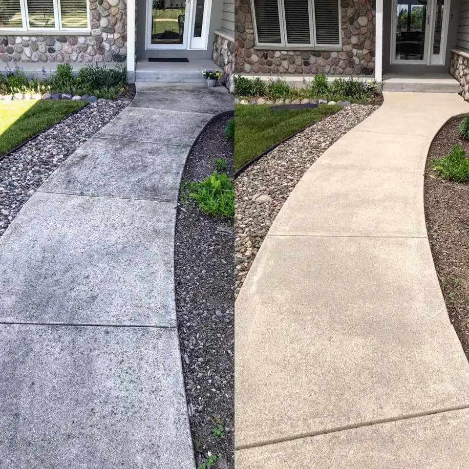 Comparison of a concrete sidewalk with a smooth finish on the left and a textured, lighter-colored concrete sidewalk on the right, separated by a landscaped strip with small rocks and plants.