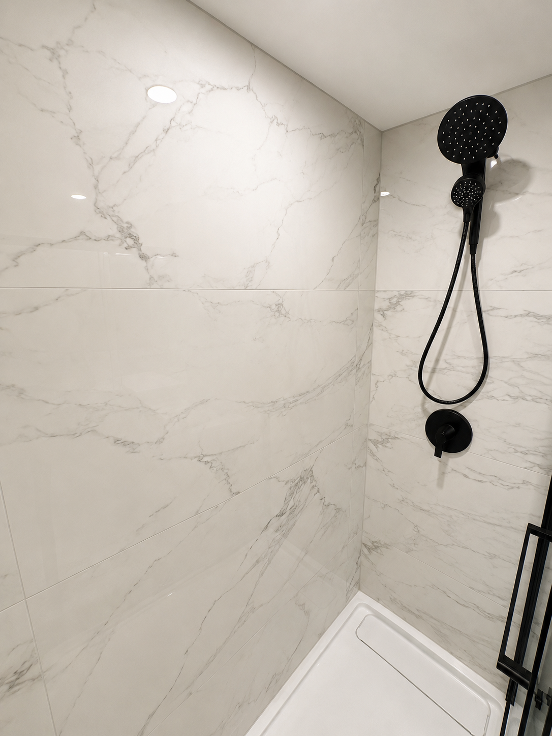 Large-format marble-look porcelain tile with matte black shower fixtures.