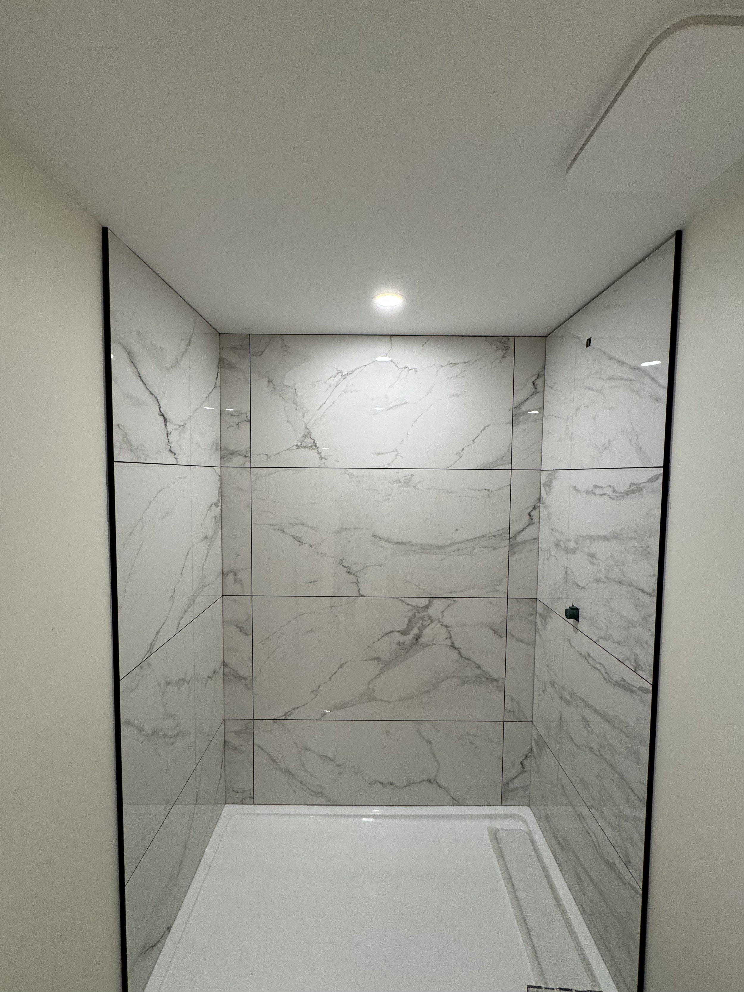 Walk-in shower with large-format porcelain tile installation.