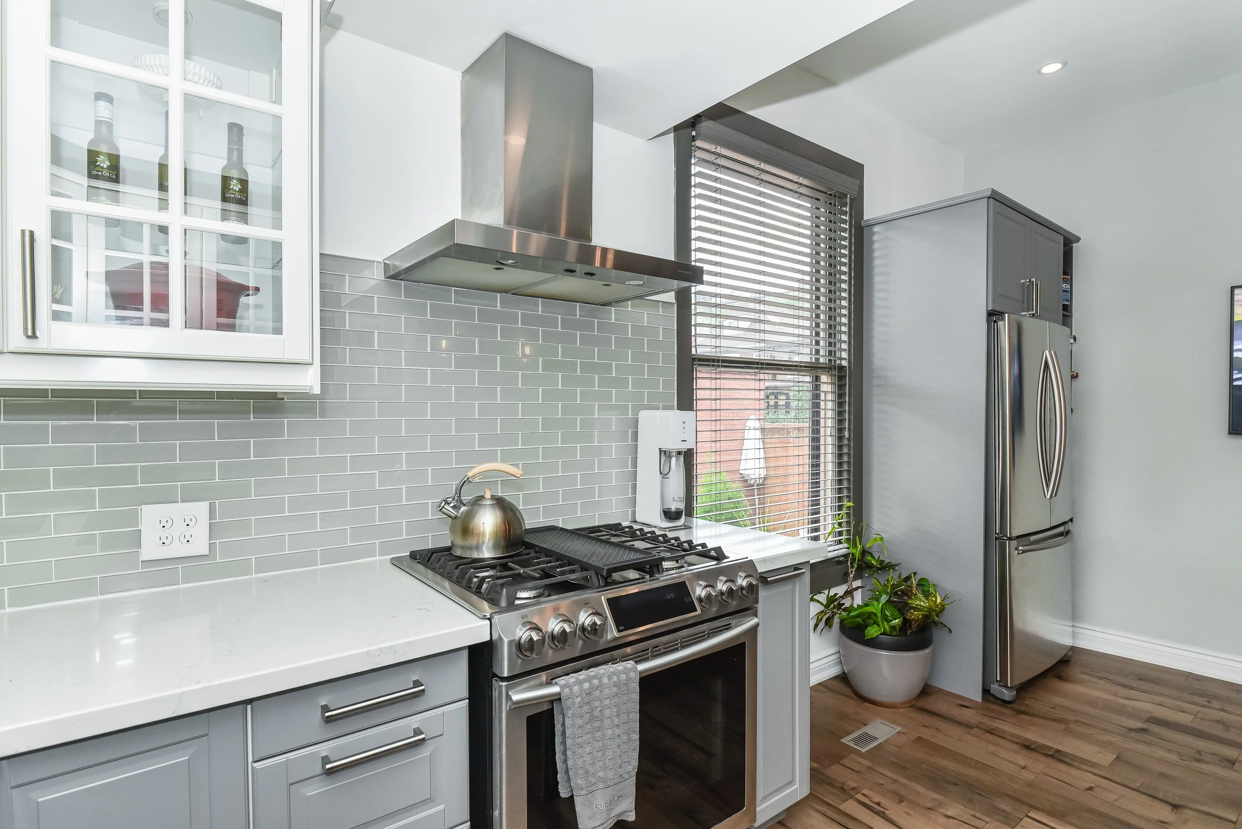 Modern kitchen with stainless steel range hood, glass backsplash tile and custom cabinetry.