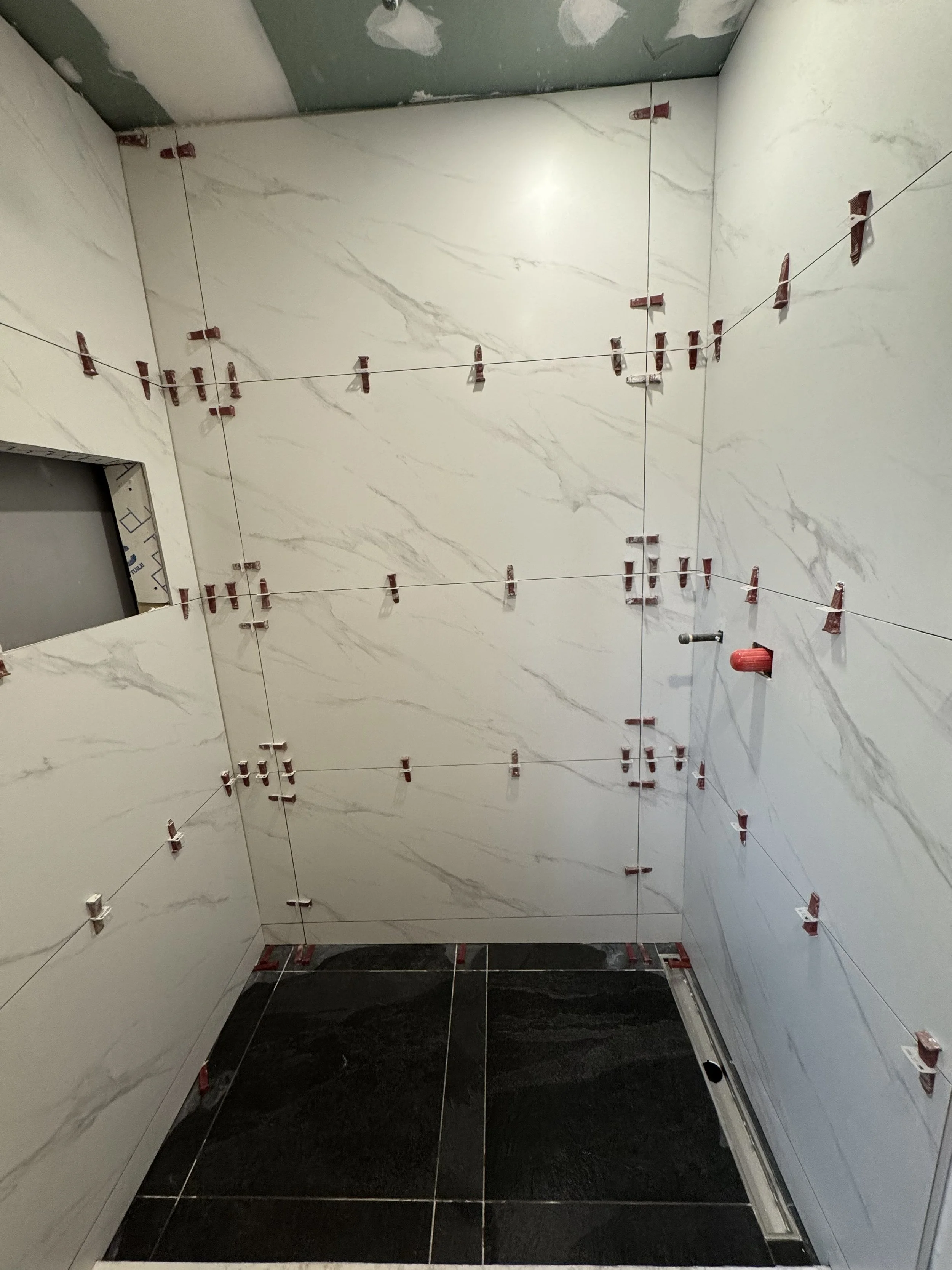 Large-format shower tile being installed on walls. 