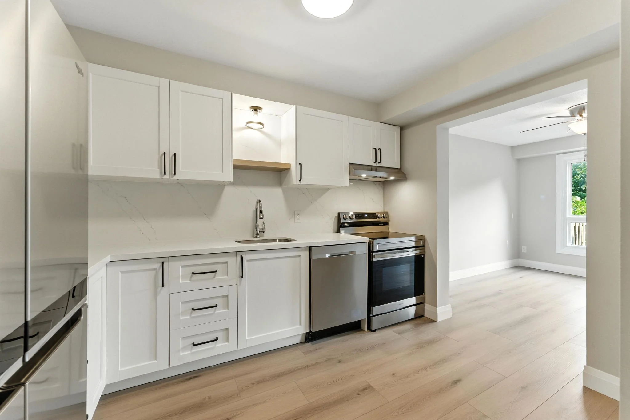 Modern kitchen renovation featuring custom white cabinetry, quartz countertop and backsplash, with an efficient open layout