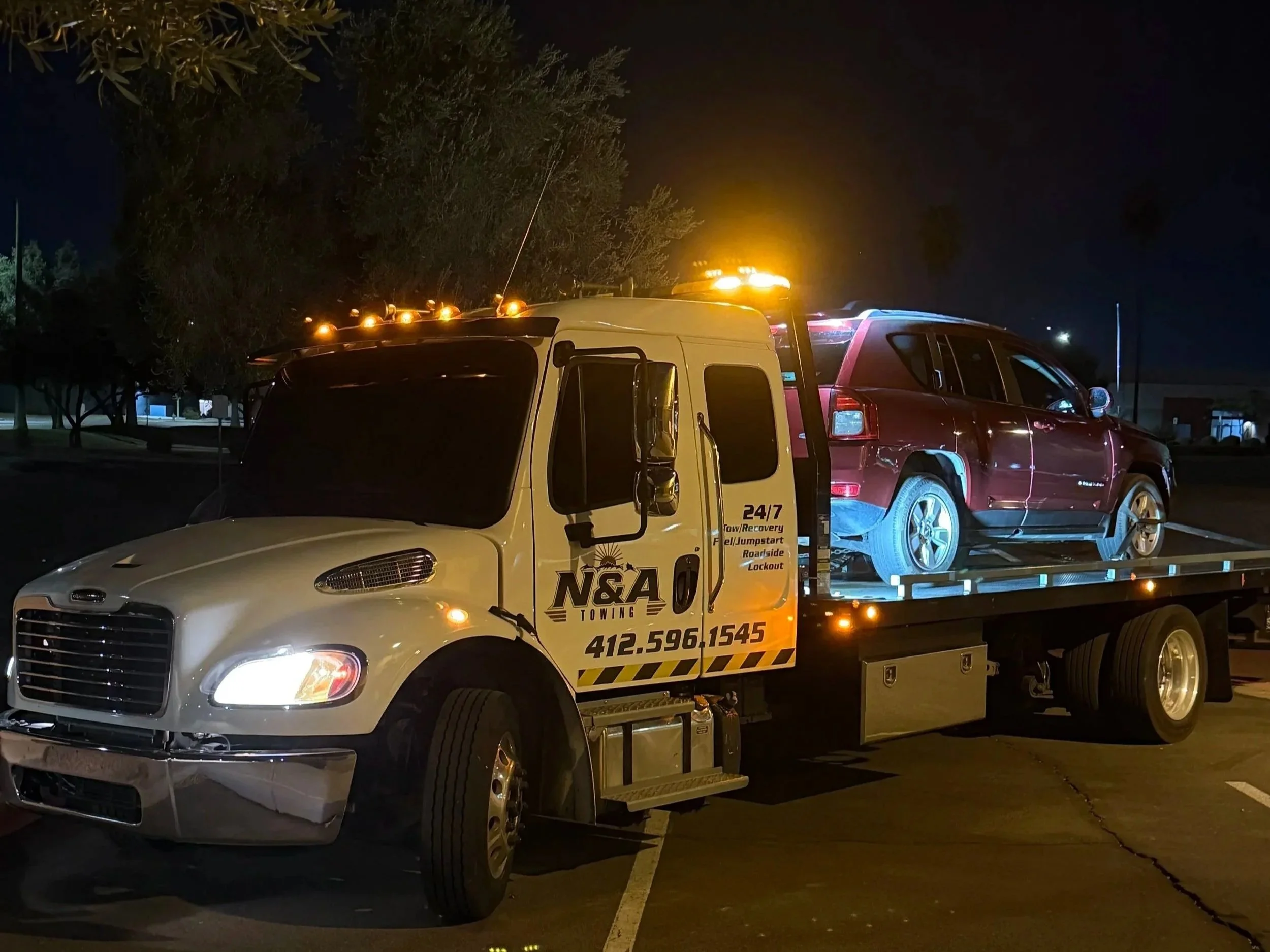 White N&A Towing rollback carrying a red SUV at night