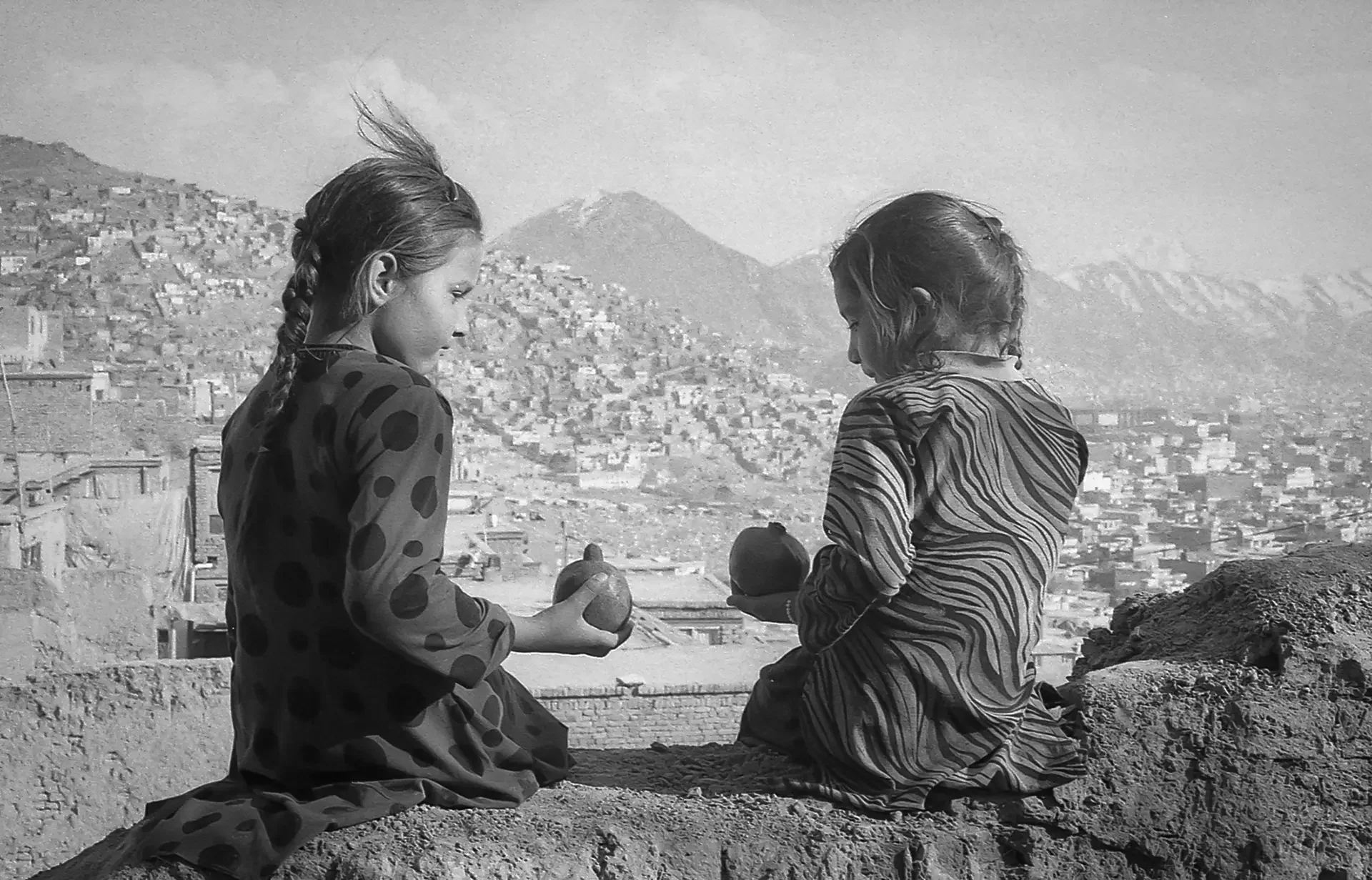 Documentary portrait of two children sitting together with a cityscape in the background, Kabul, Afghanistan.