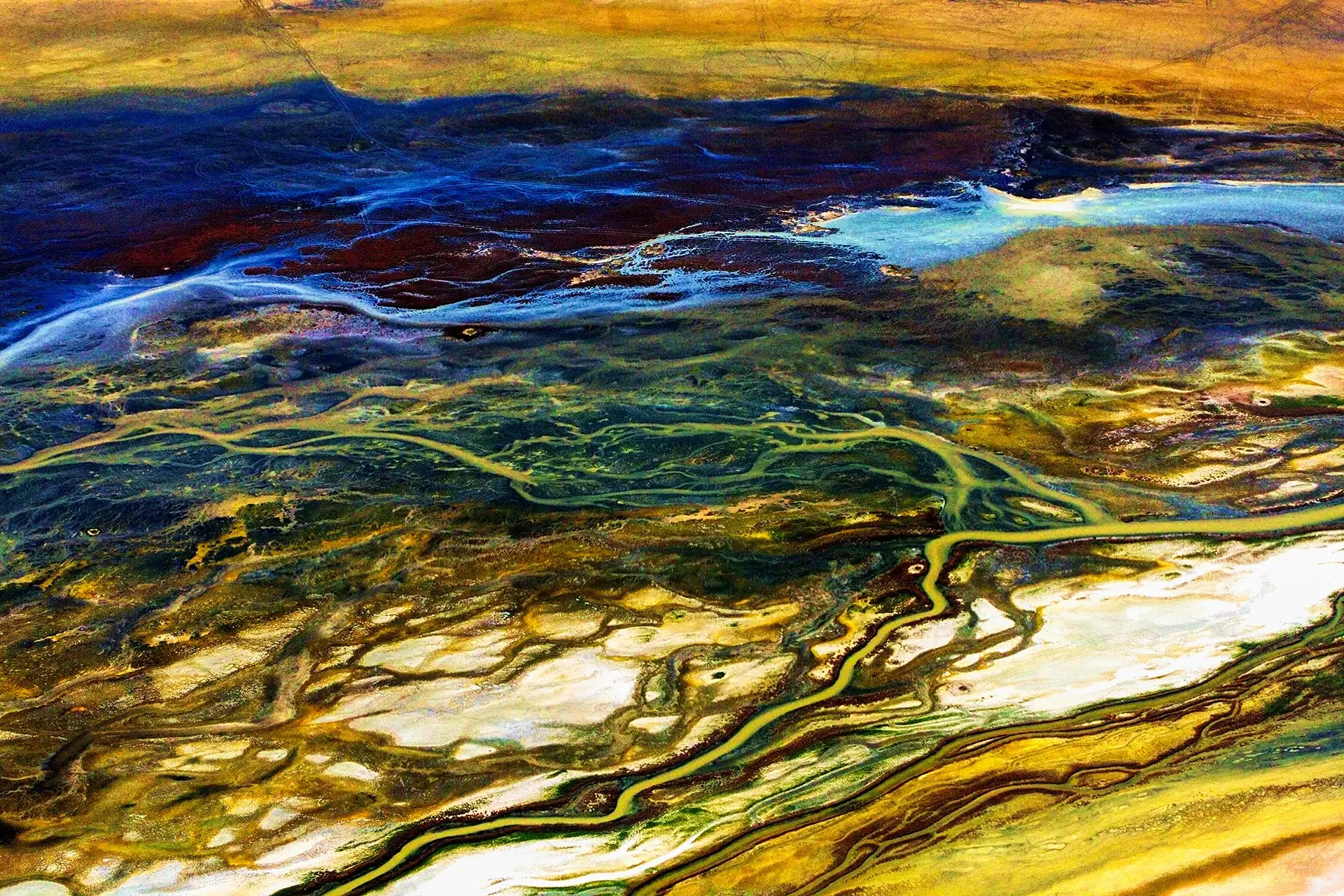 Abstract aerial landscape photography capturing fluid organic textures and golden sediment patterns of a river in Southern Iran.