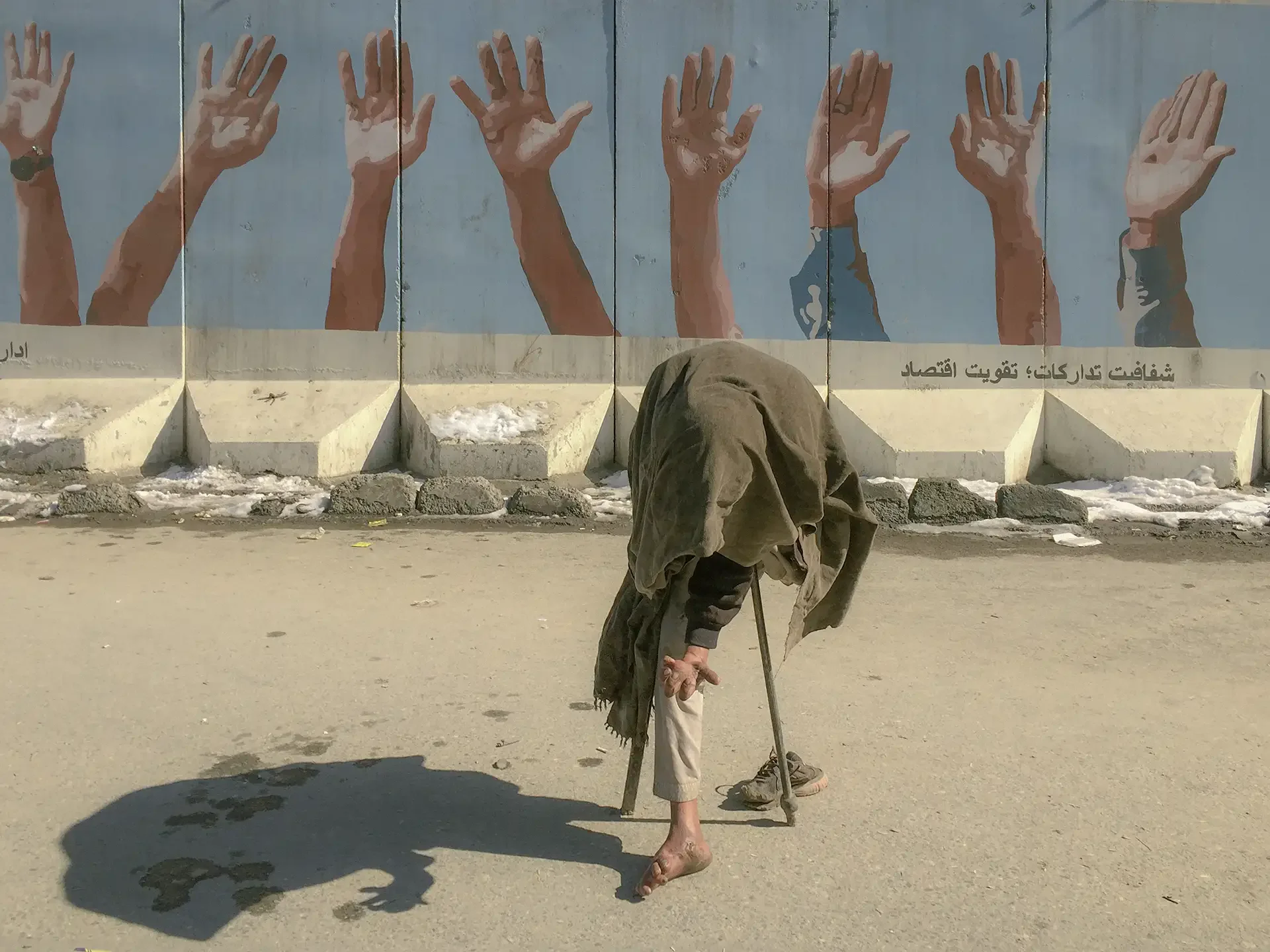 street photography capturing a person walking past a mural of hands, Kabul, Afghanistan.⁠