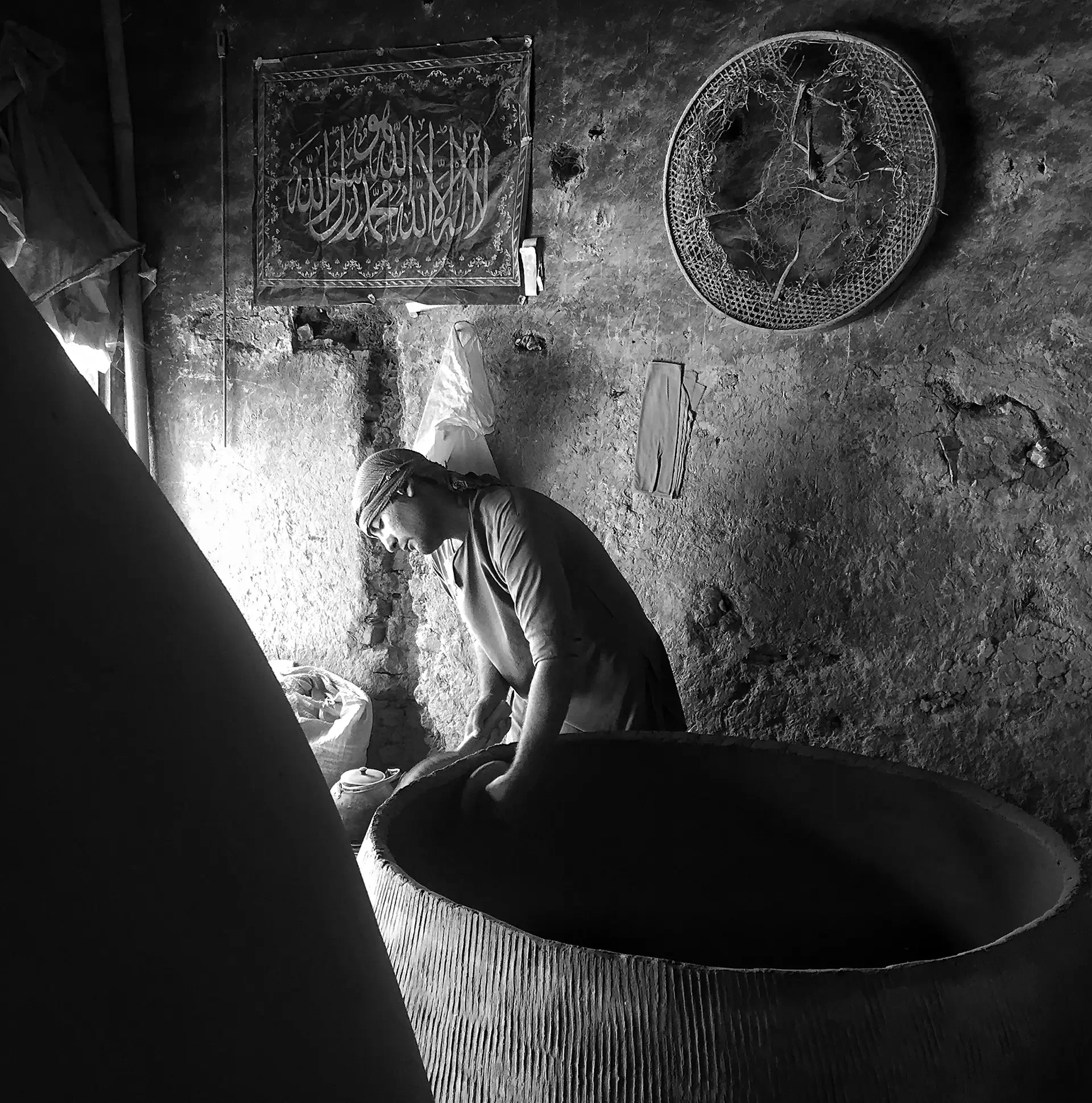 High-contrast black and white photography capturing a person working in a dimly lit interior, Kabul, Afghanistan.