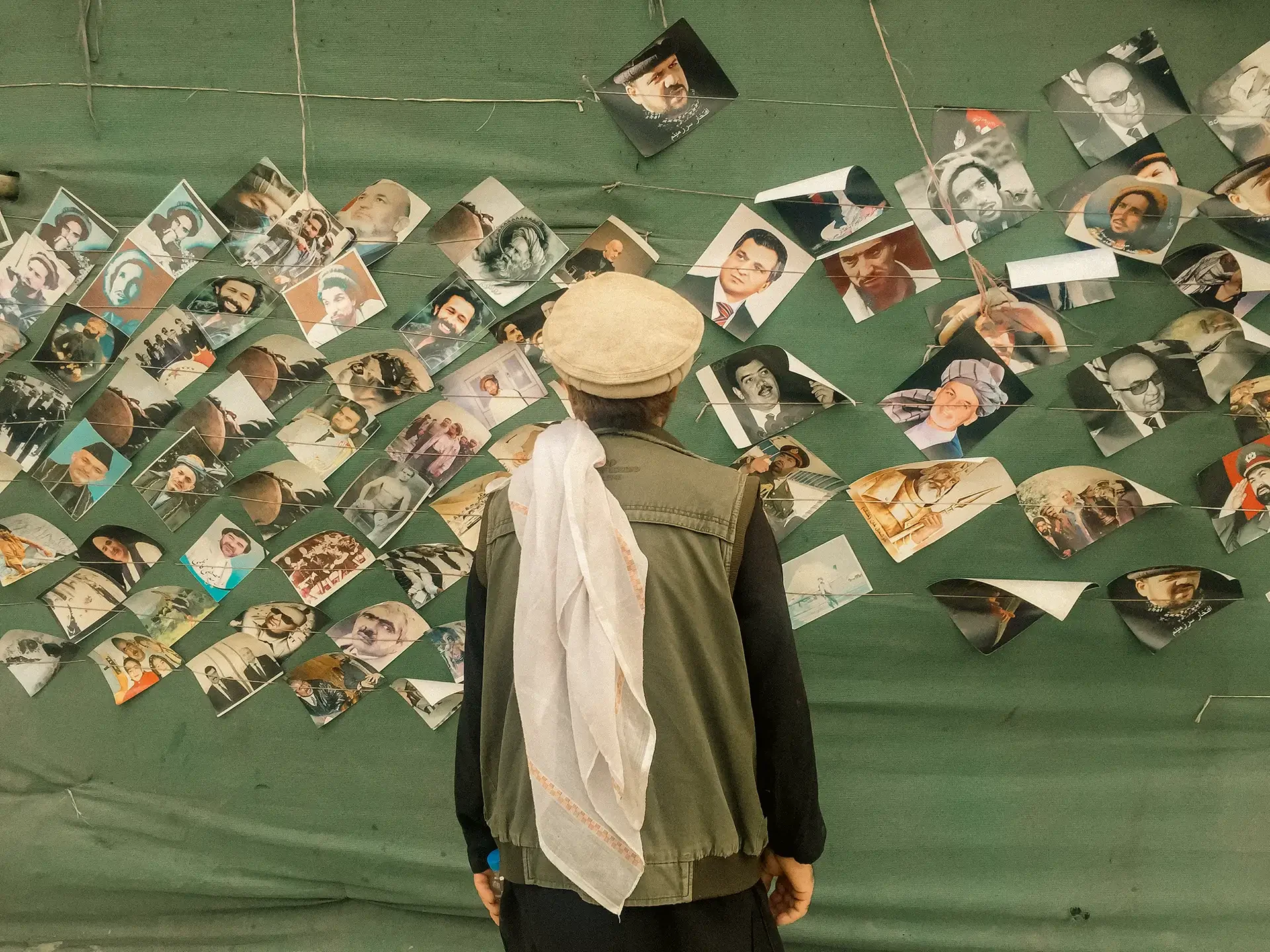 Minimalist documentary scene focusing on a person in front of a photo display wall, Shahreno, Kabul, Afghanistan.⁠