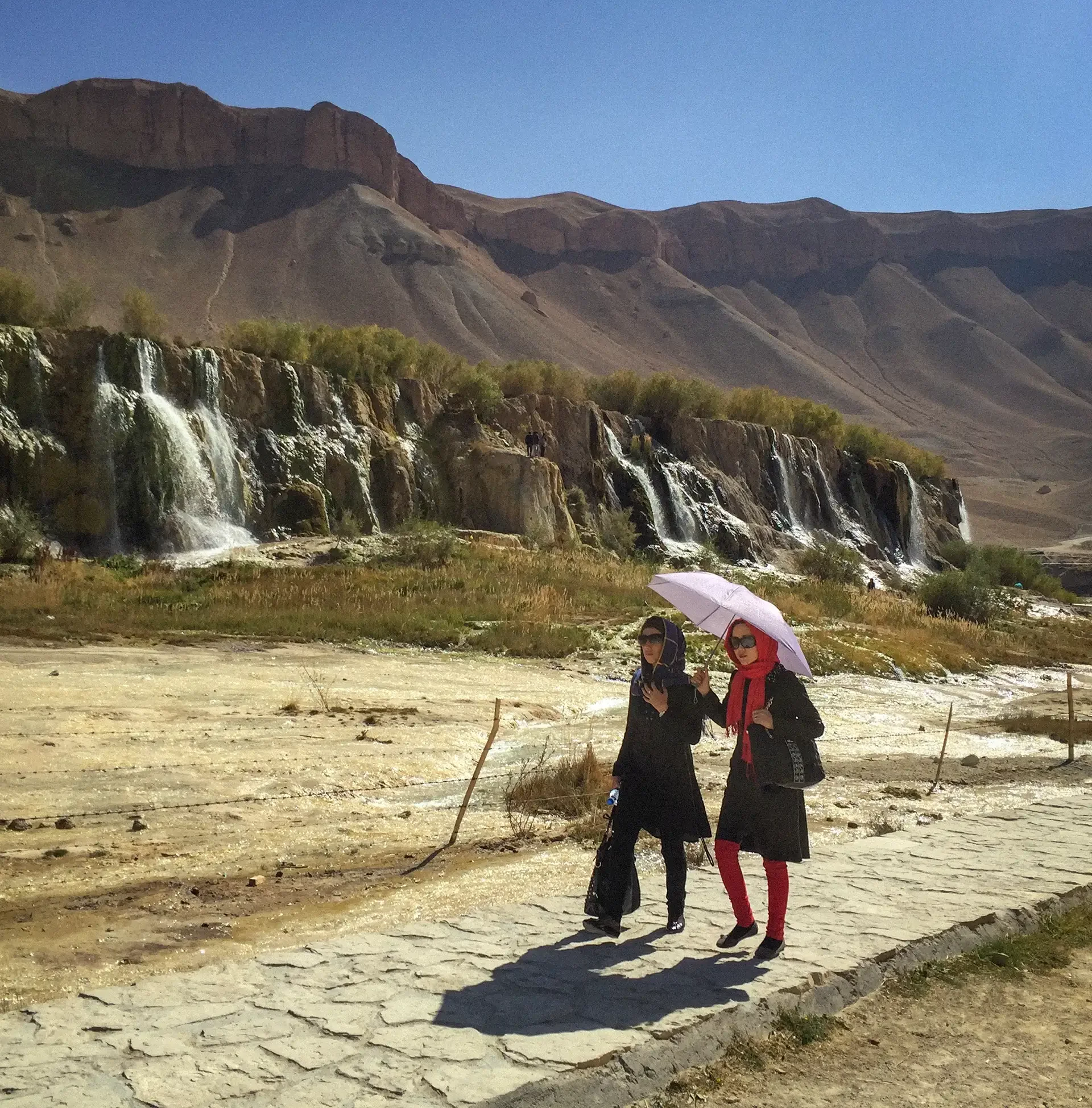 Documentary landscape photography capturing people walking near a natural cliffside waterfall,Bande Amir, Bamian, Afghanistan.
