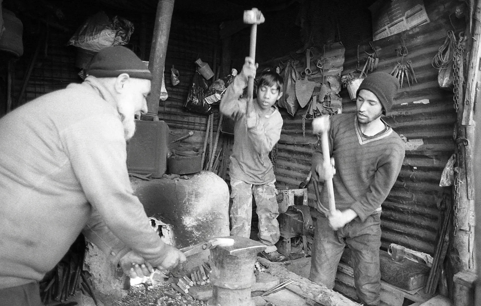 Black and white documentary photography capturing blacksmiths working in a traditional workshop, Mandavi, Kabul, Afghanistan.