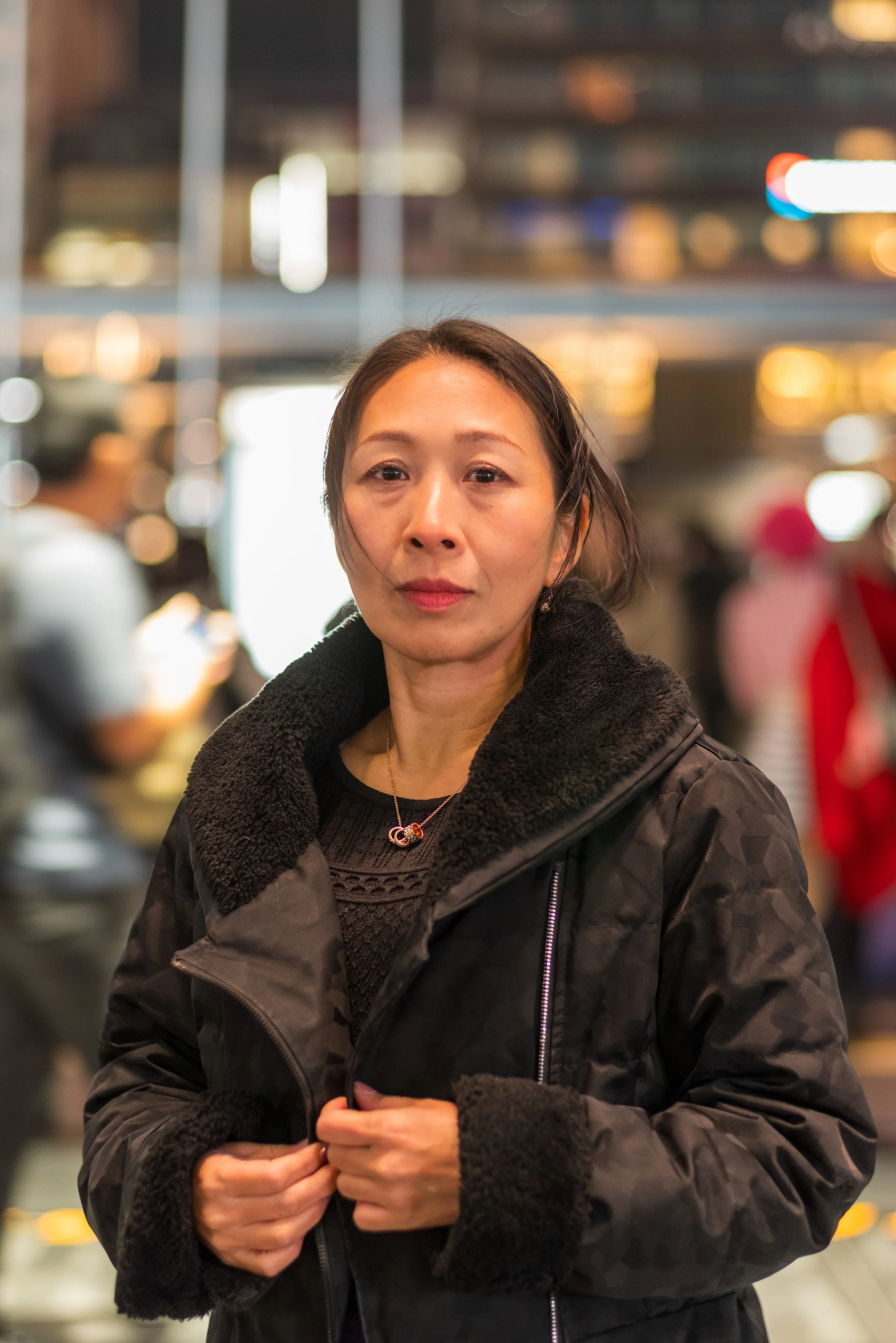 夜の都市で女性が立っている。背後にはぼやけた街の灯りがある。