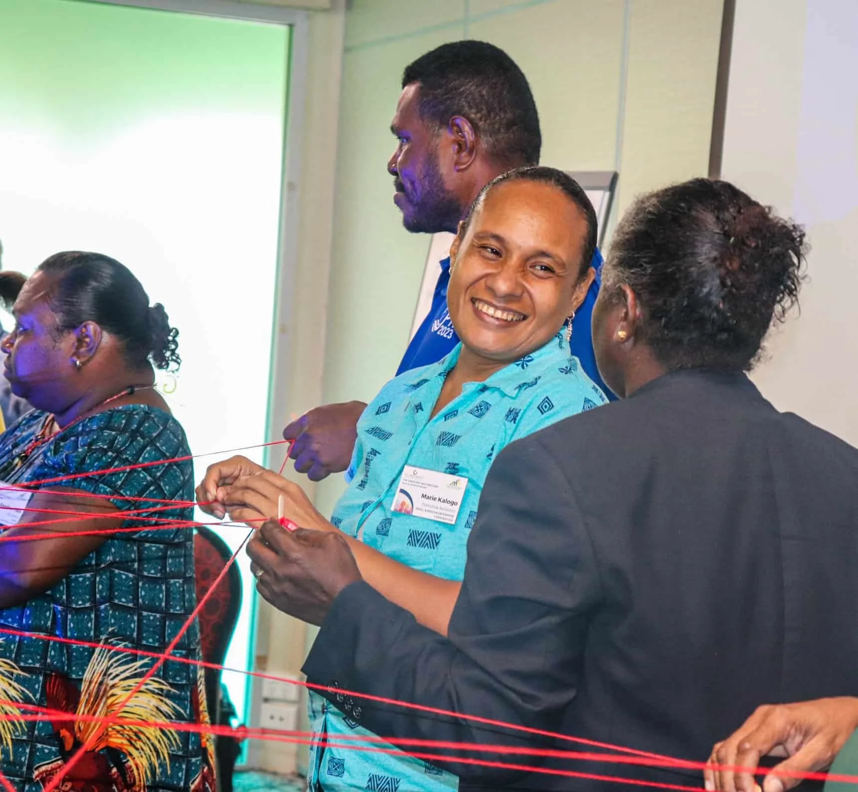 Group of diverse people participating in a team-building activity involving red string, smiling and engaging with each other indoors.