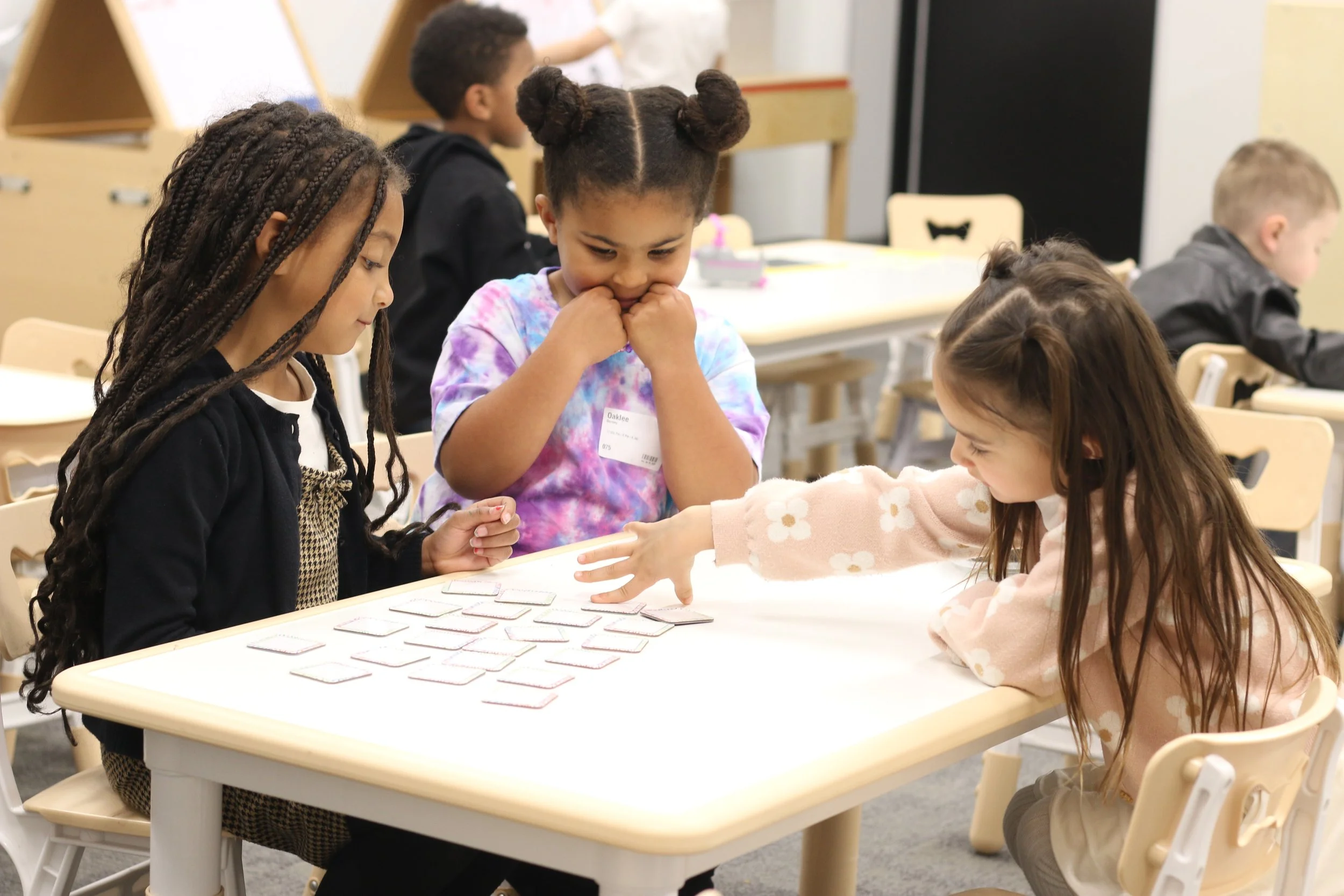 A group of children sitting around a table playing a card game in a classroom.