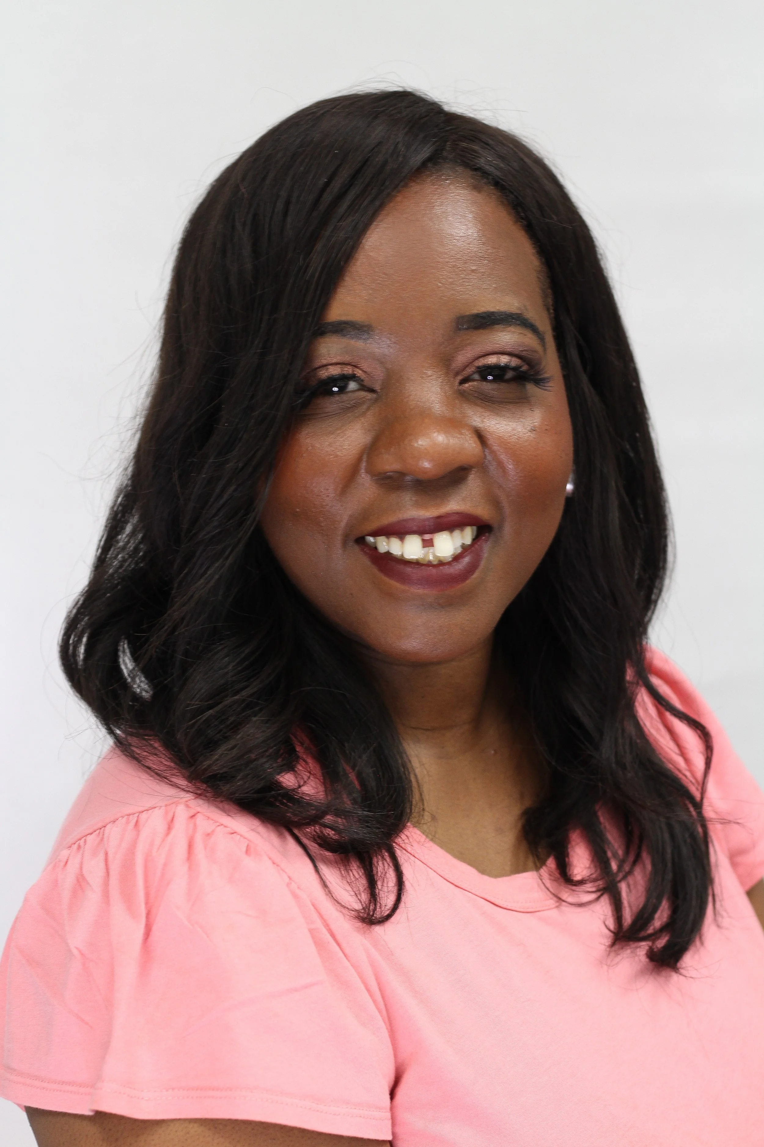 A smiling woman with dark hair wearing a pink shirt against a white background.