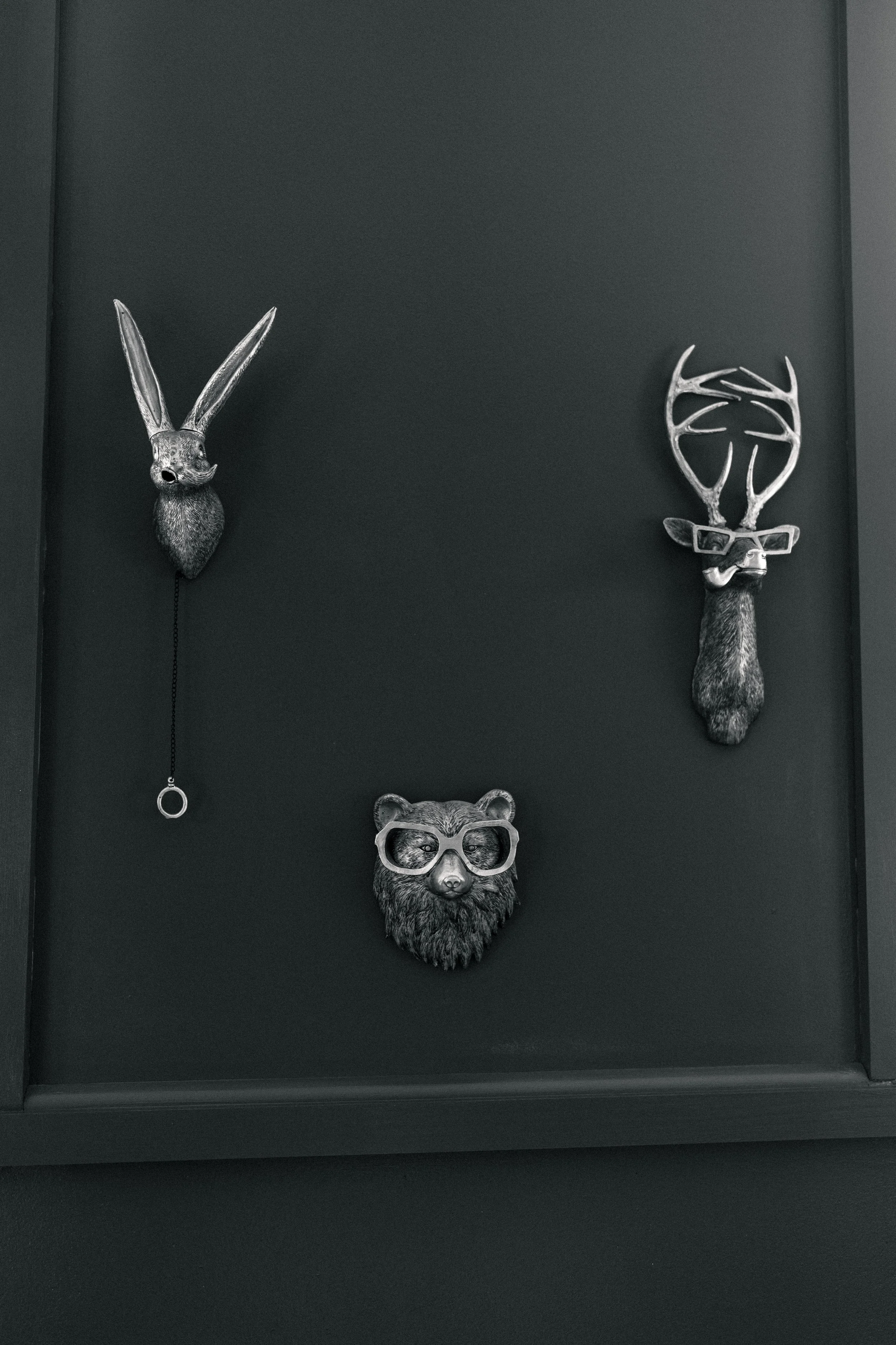 Decorative animal head wall art set including a rabbit on the left, a bear in the center with glasses, and a stag on the right with glasses and a pipe, all mounted on a dark wall.