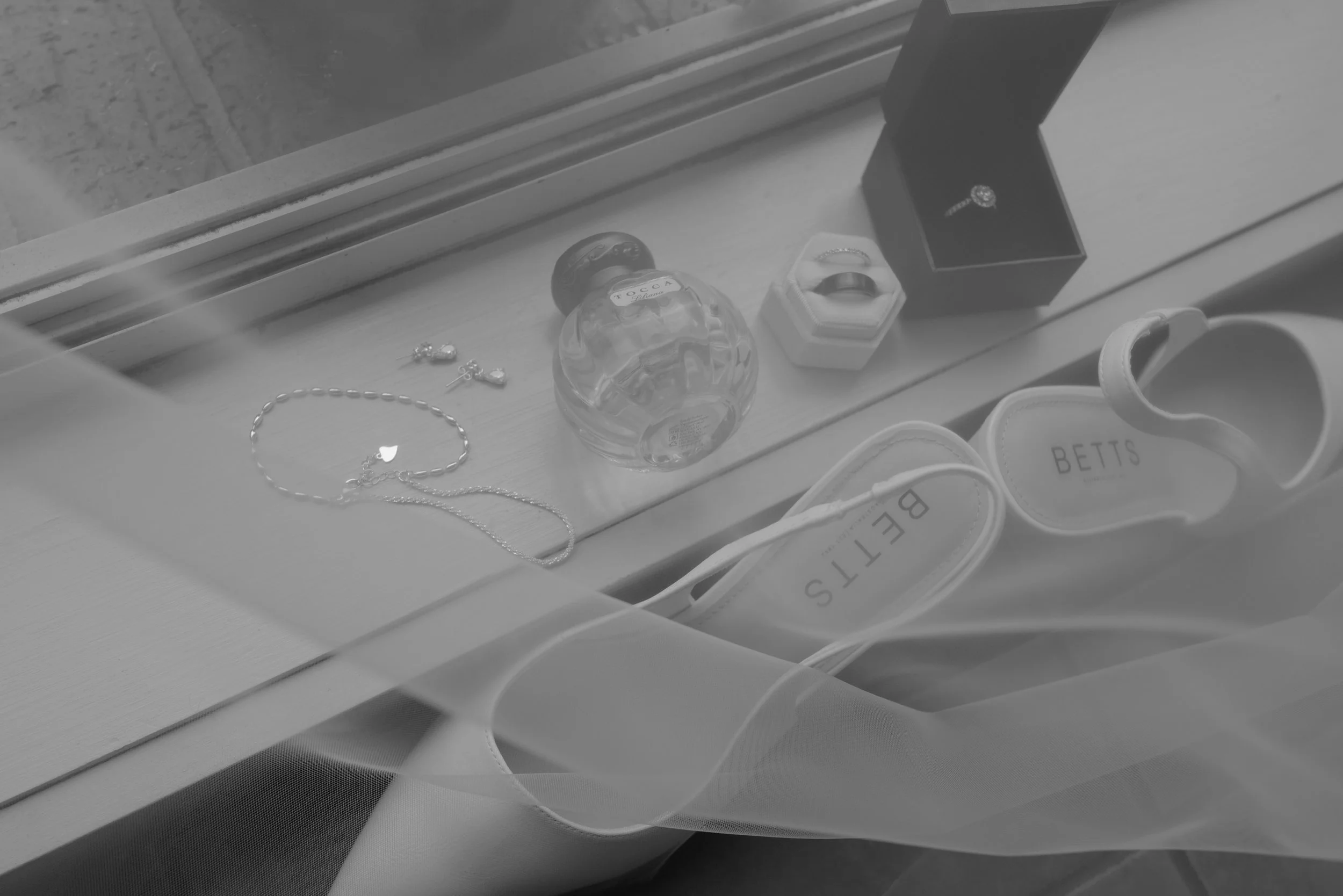 Jewelry, perfume, shoes, and a ring displayed on a windowsill behind a glass pane.