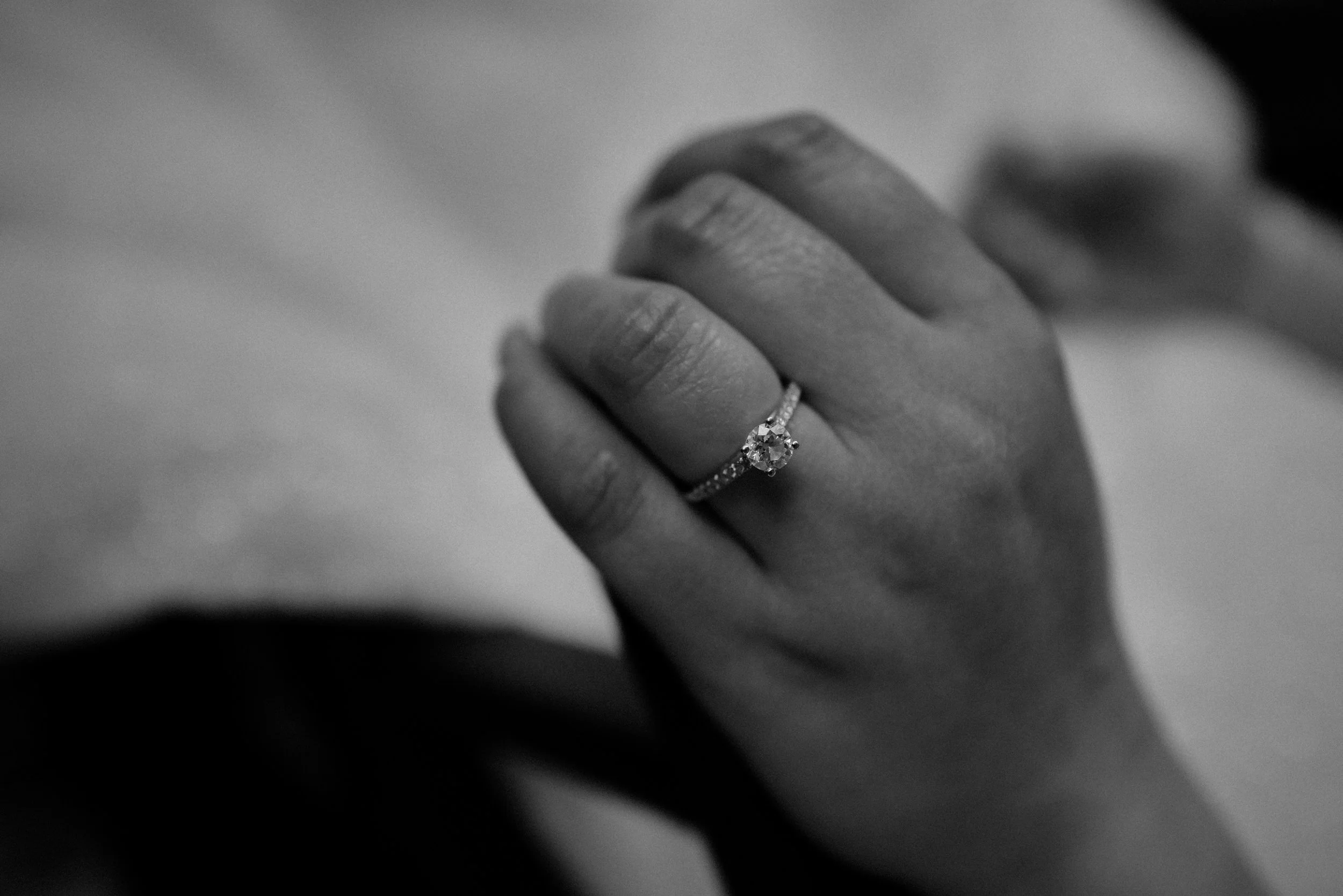 Close-up of a person's hand wearing an engagement ring with a large central diamond and smaller diamonds on the band.