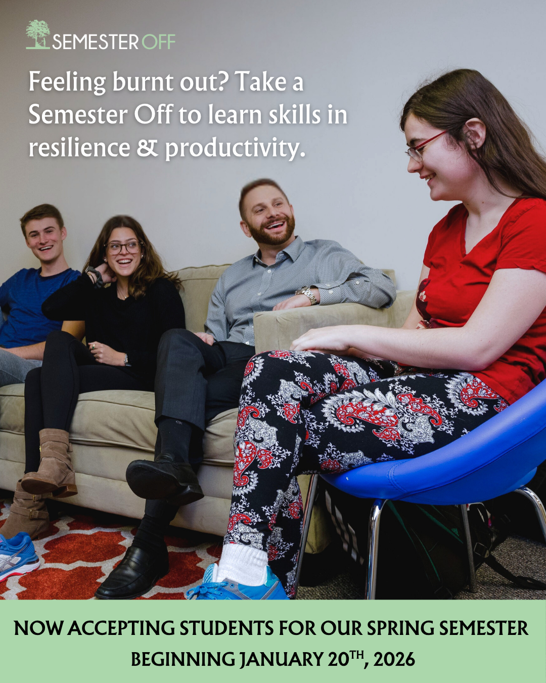 Group of four young adults sitting on a couch and chair, smiling and engaging in conversation, with a plain wall in the background.