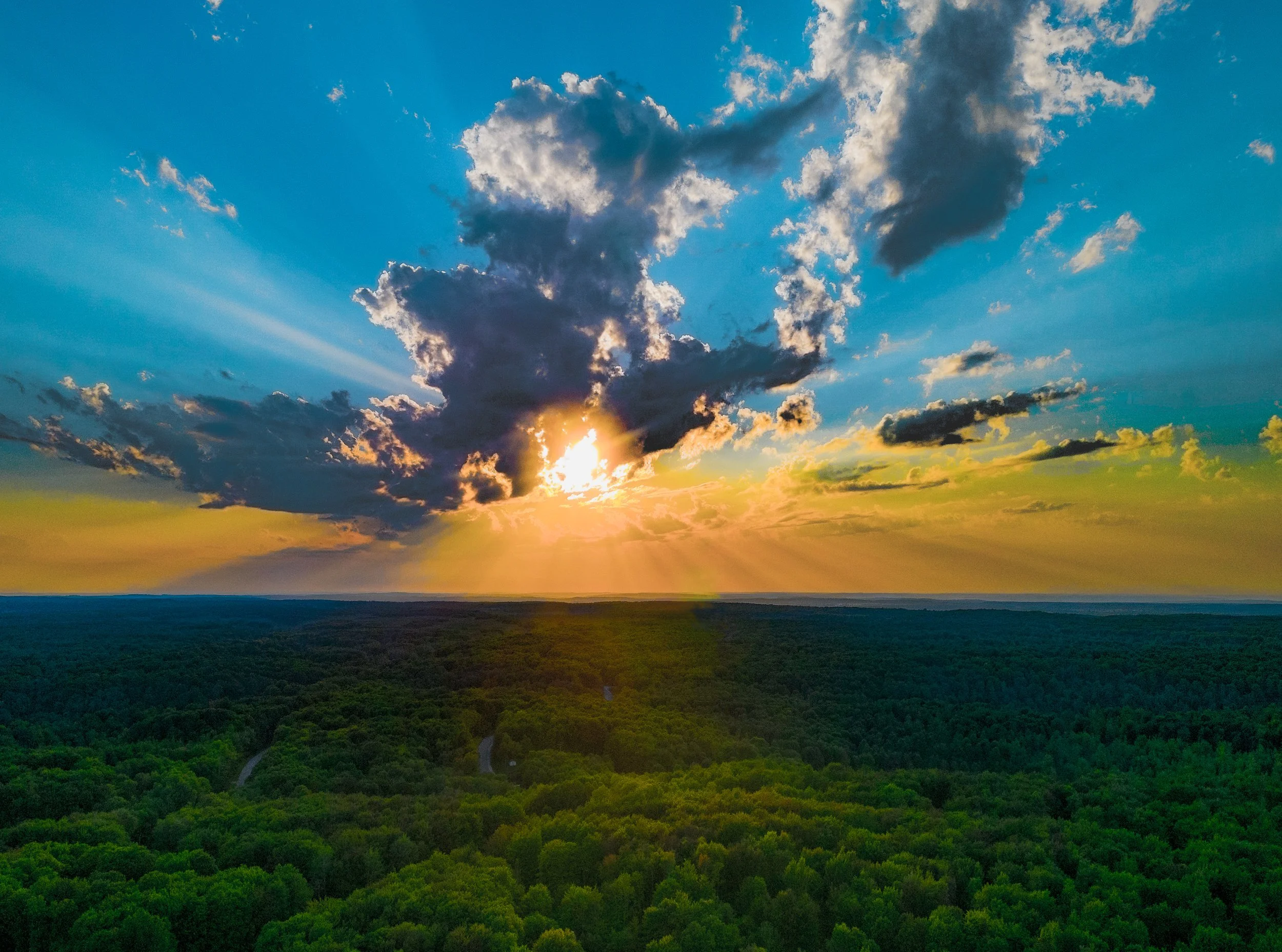 Sunset over a lush green forest with a winding path and a partially cloudy sky at Lakes of the North, between Gaylord and Mancelona, Michigan.