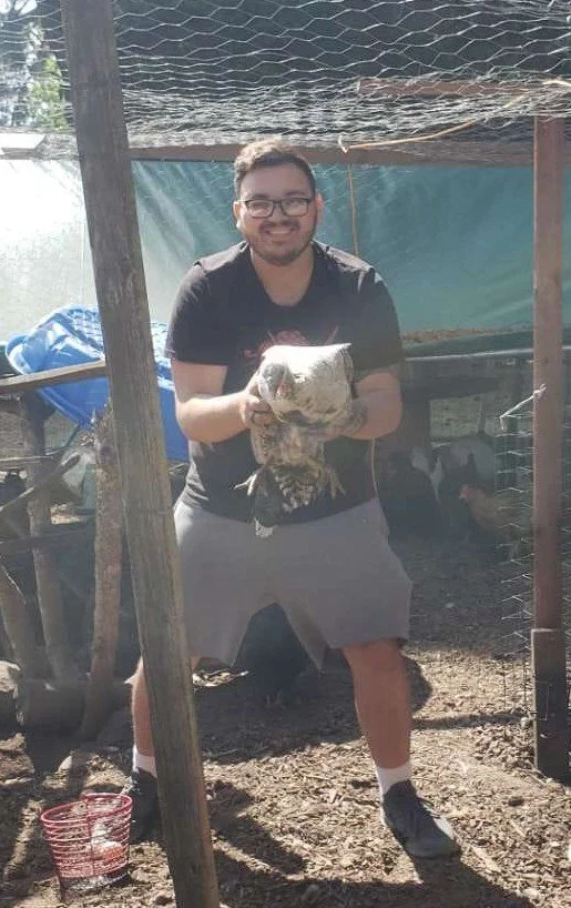 A man smiling and holding a large bird or poultry in an outdoor farm or coop.