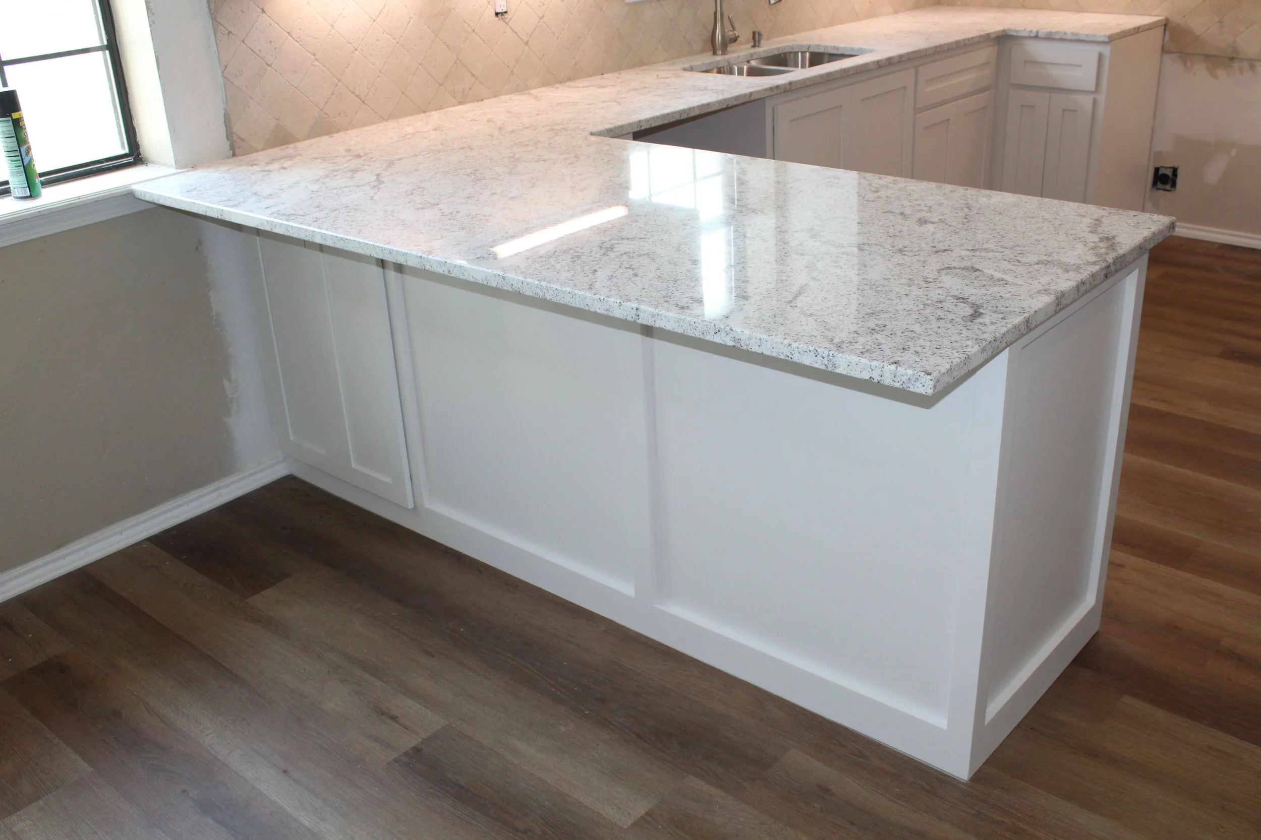 New kitchen with white cabinets, a granite countertop, stainless steel sink, and wood flooring.