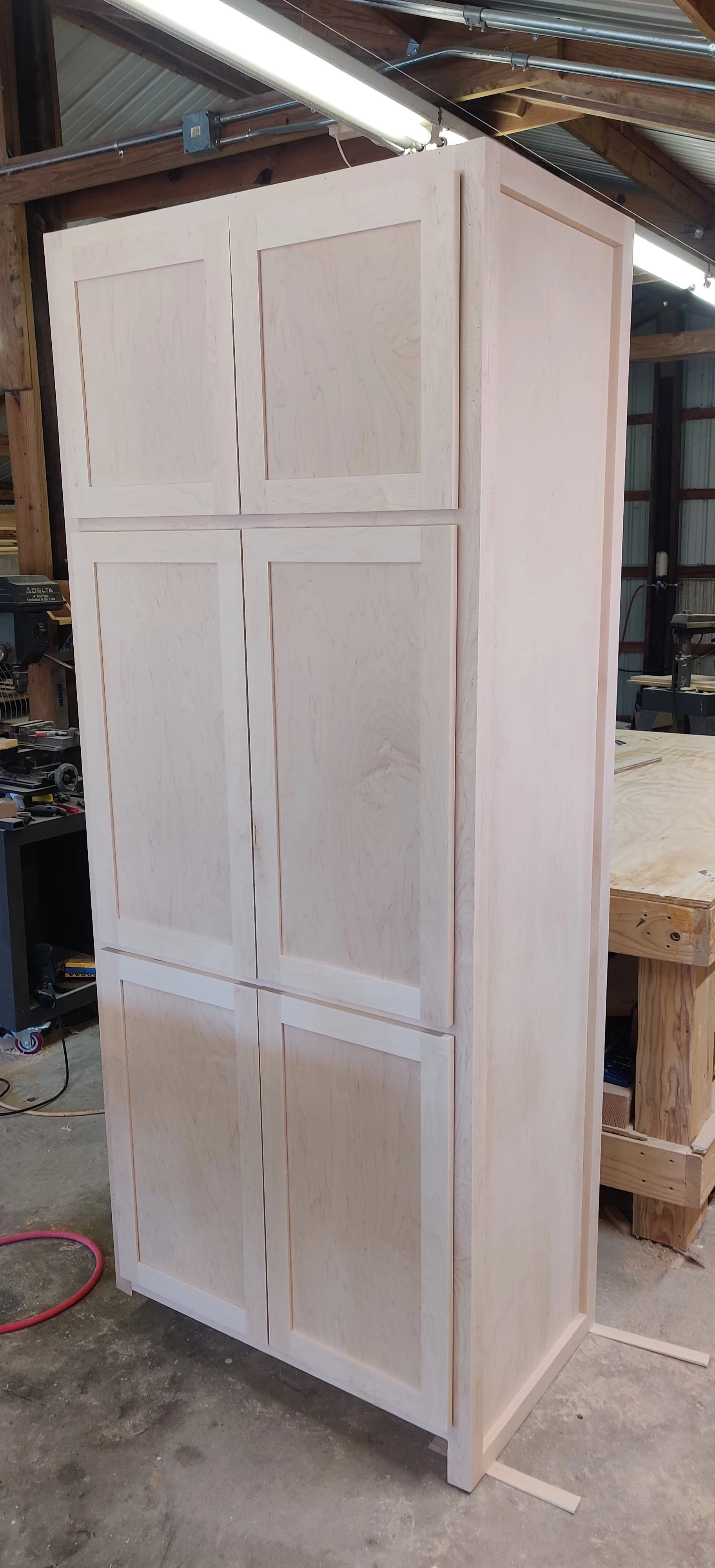 Unfinished wooden cabinet in a woodworking shop with tools and woodworking equipment around.