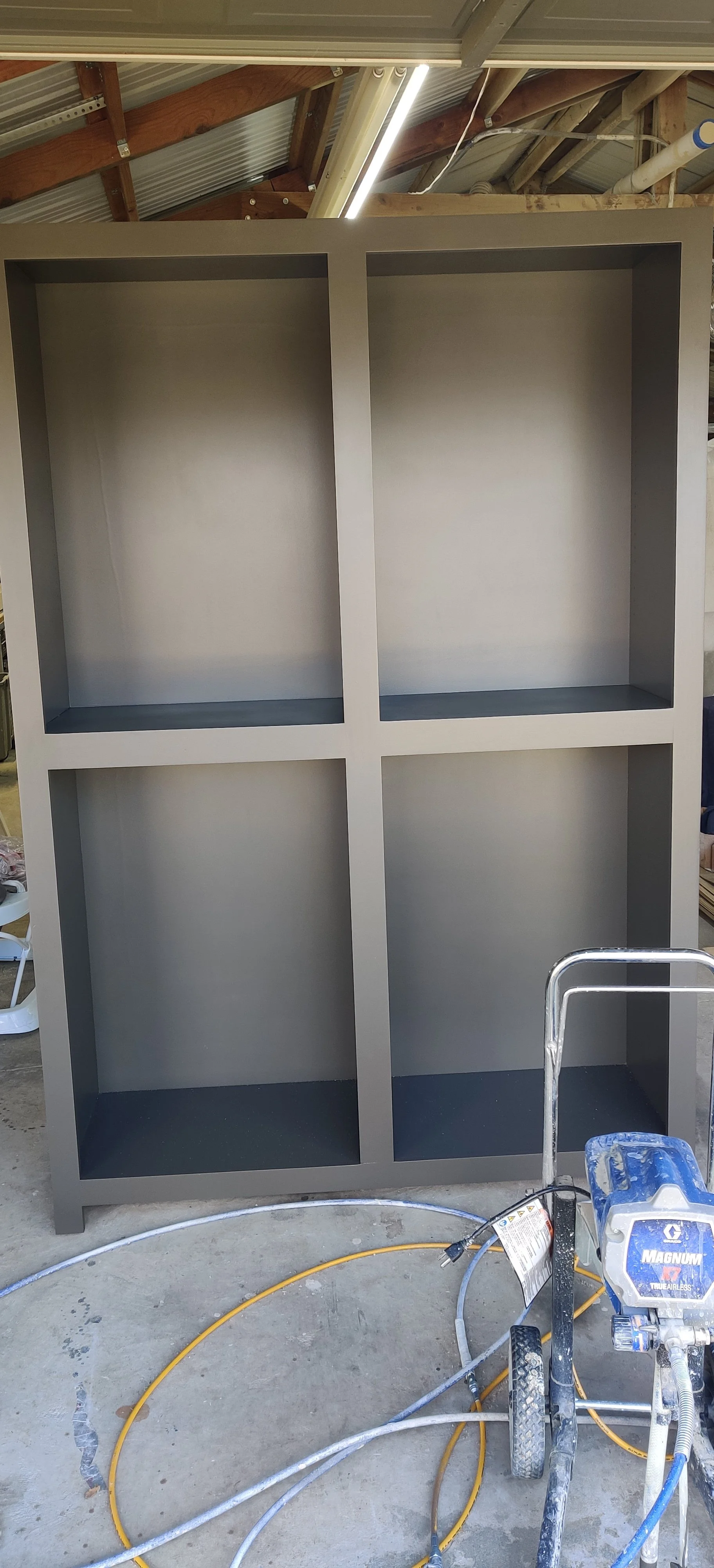 Unfinished gray bookshelf with four compartments in a workshop.