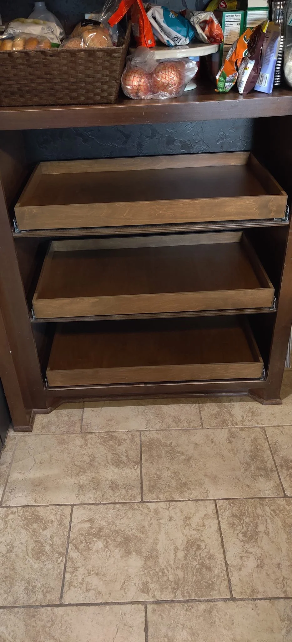 Empty kitchen cabinet with open wooden shelves, above a tiled floor.