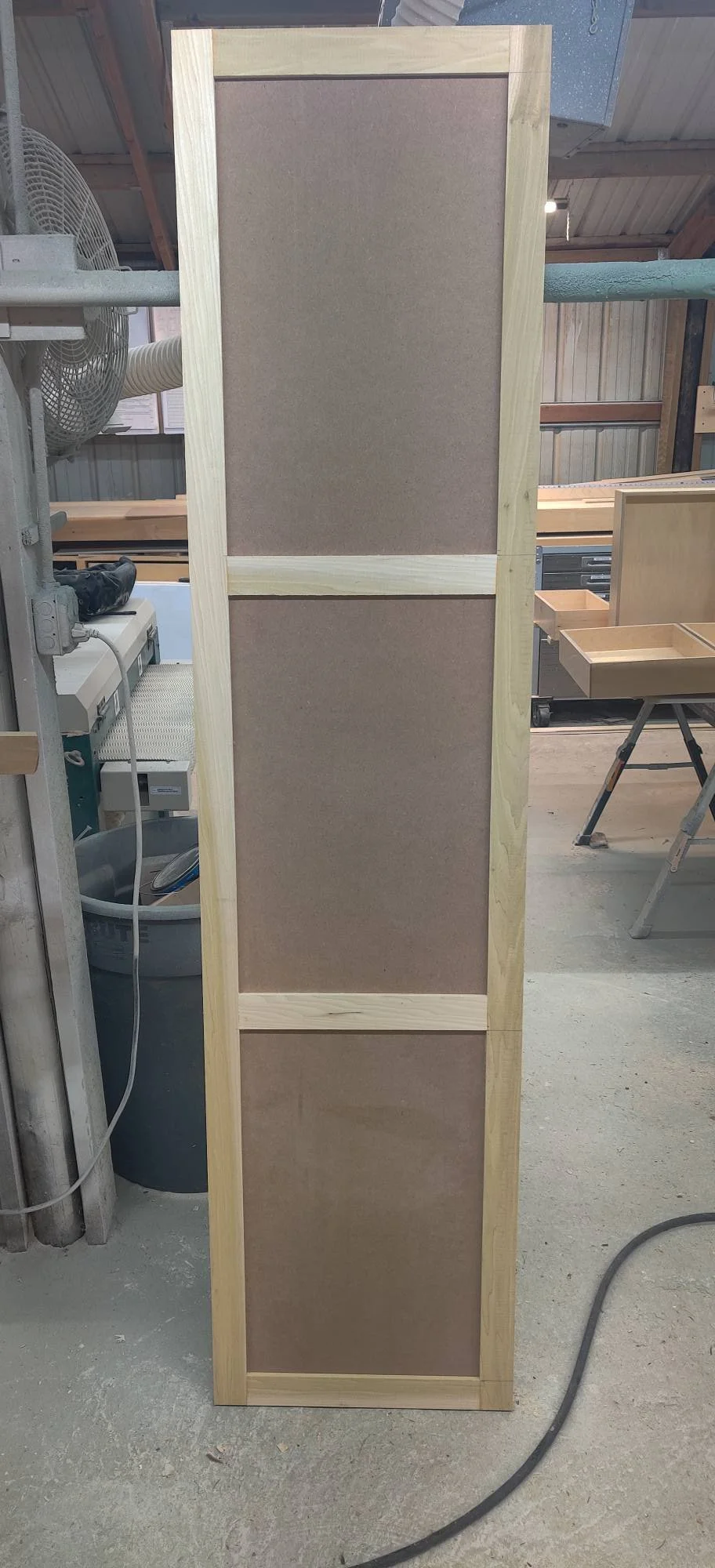 A tall wooden shelf unit with three brown fabric-covered panels in a workshop.