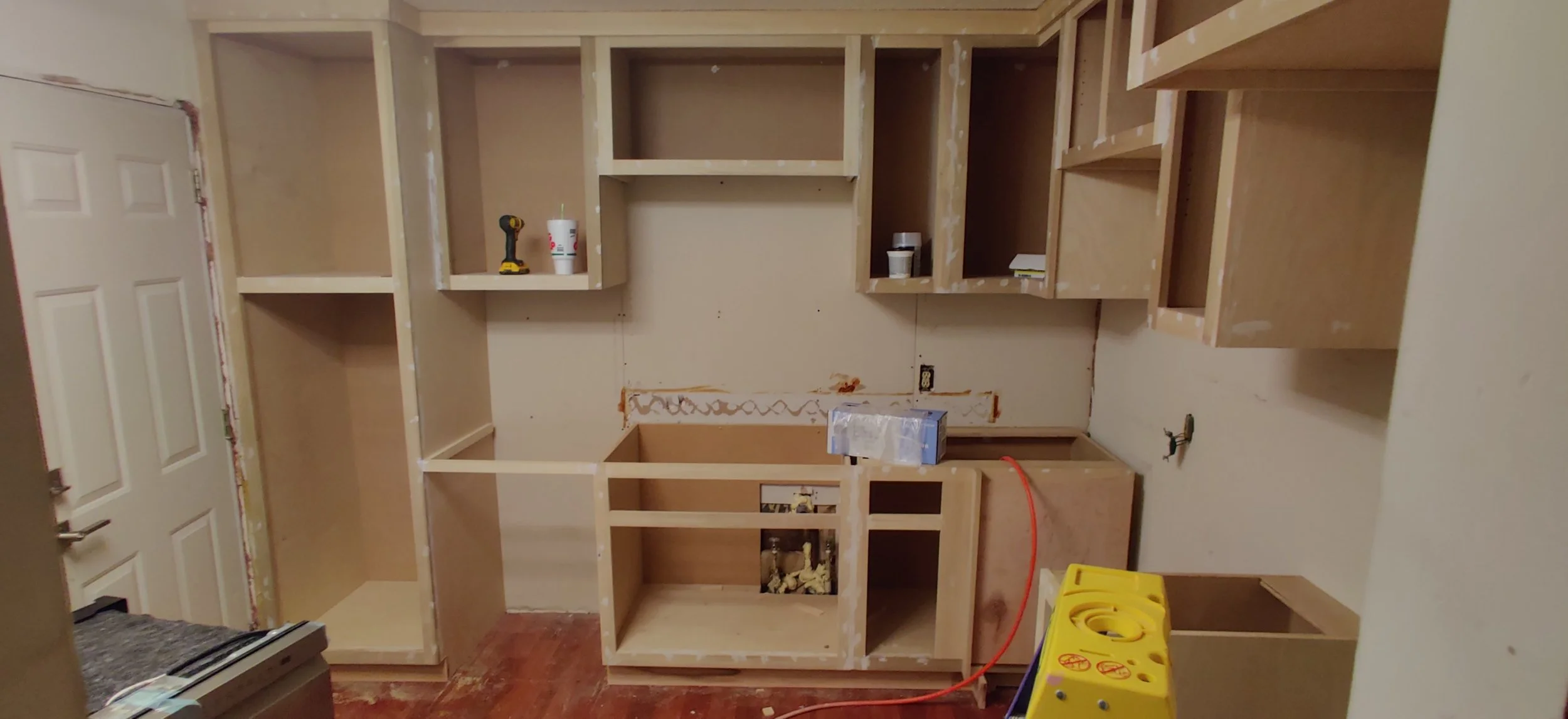 Unfinished kitchen cabinetry with wooden frames and open shelves under construction, tools and supplies visible.