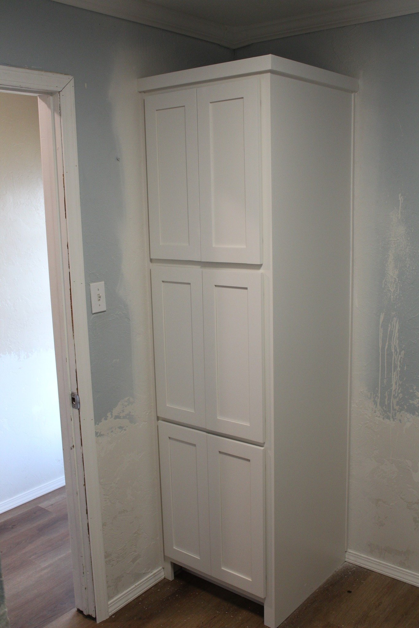 White built-in corner cabinet with two doors, situated in a room with gray textured walls and white trim.