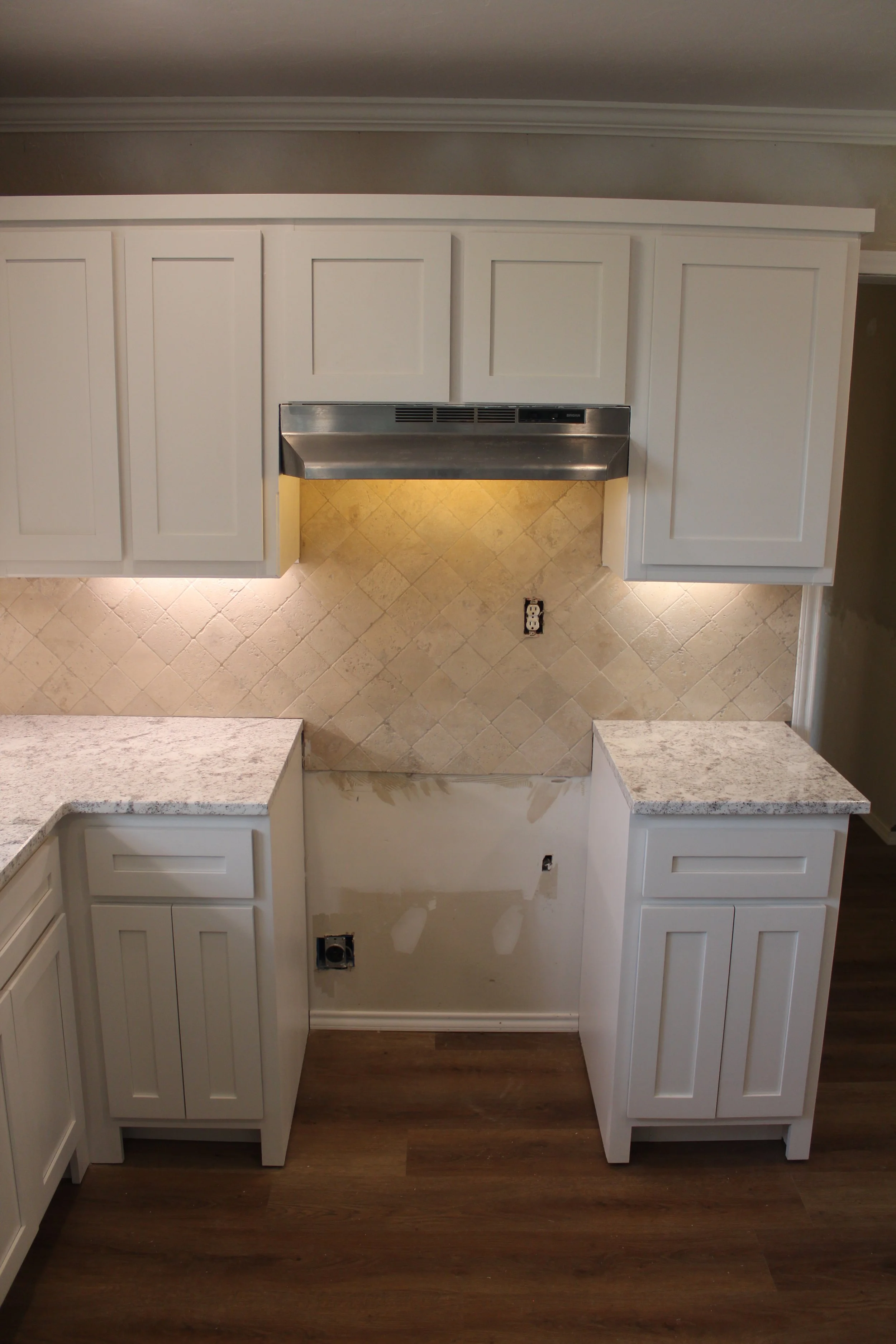 Kitchen cabinets with some sections missing doors, beige tile backsplash, and dark wood flooring.
