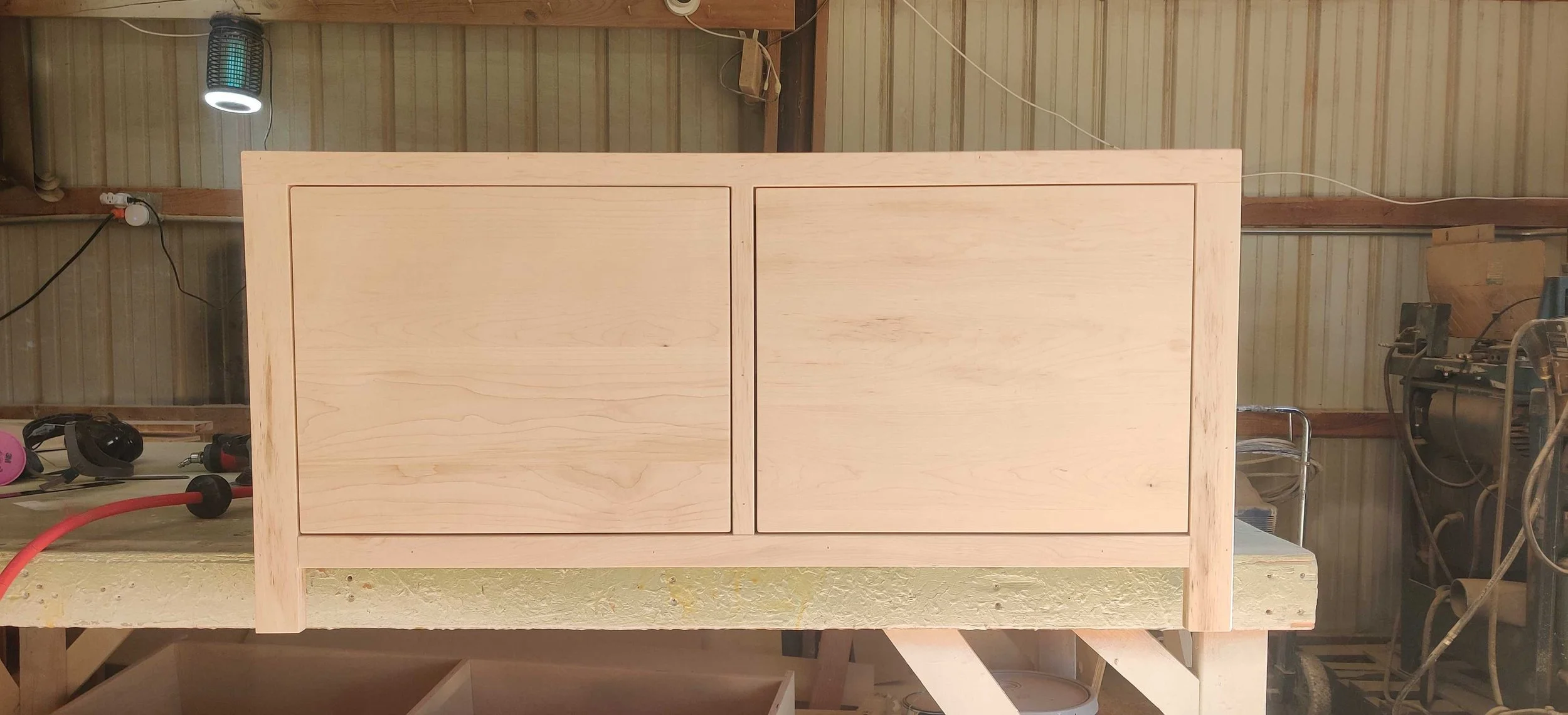 unfinished wooden cabinet with two doors in a workshop.