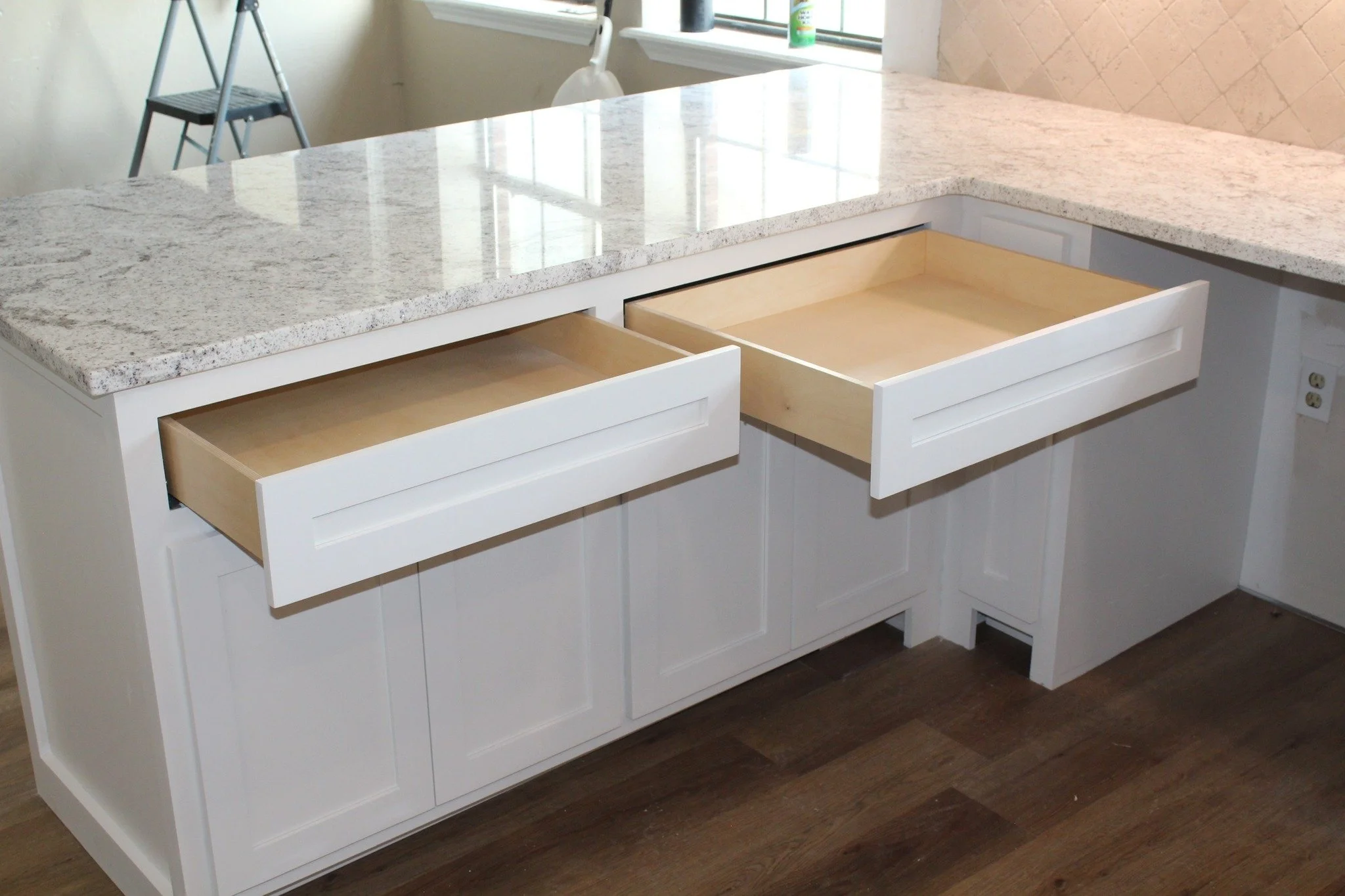 Kitchen island with a granite countertop and two open drawers, white cabinets, and a window in the background.