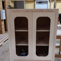 A wooden cabinet with glass-paneled doors and two shelves inside.