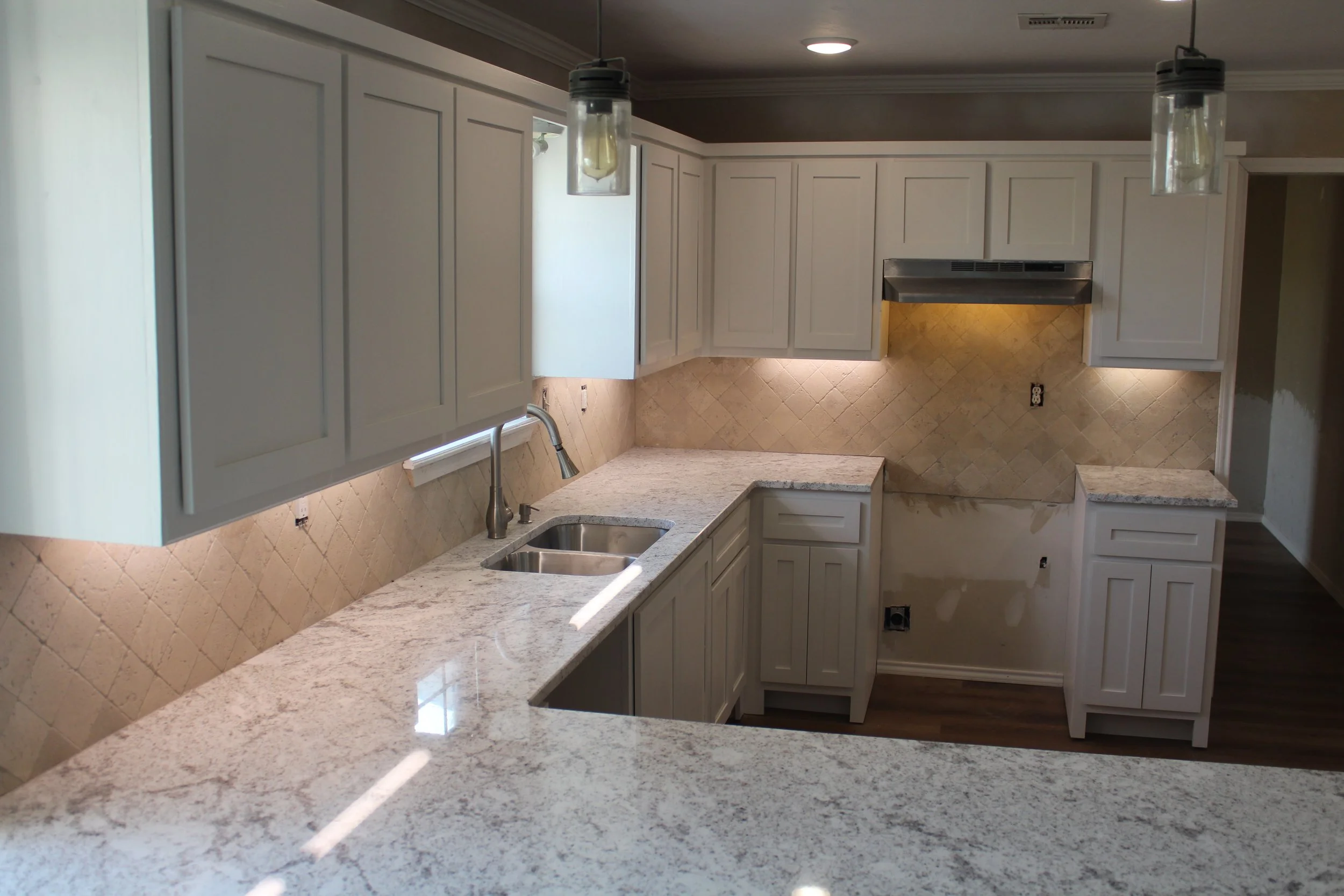 Kitchen with white cabinets, granite countertops, beige tiled backsplash, stainless steel range hood, and dual sink with brushed nickel faucet.