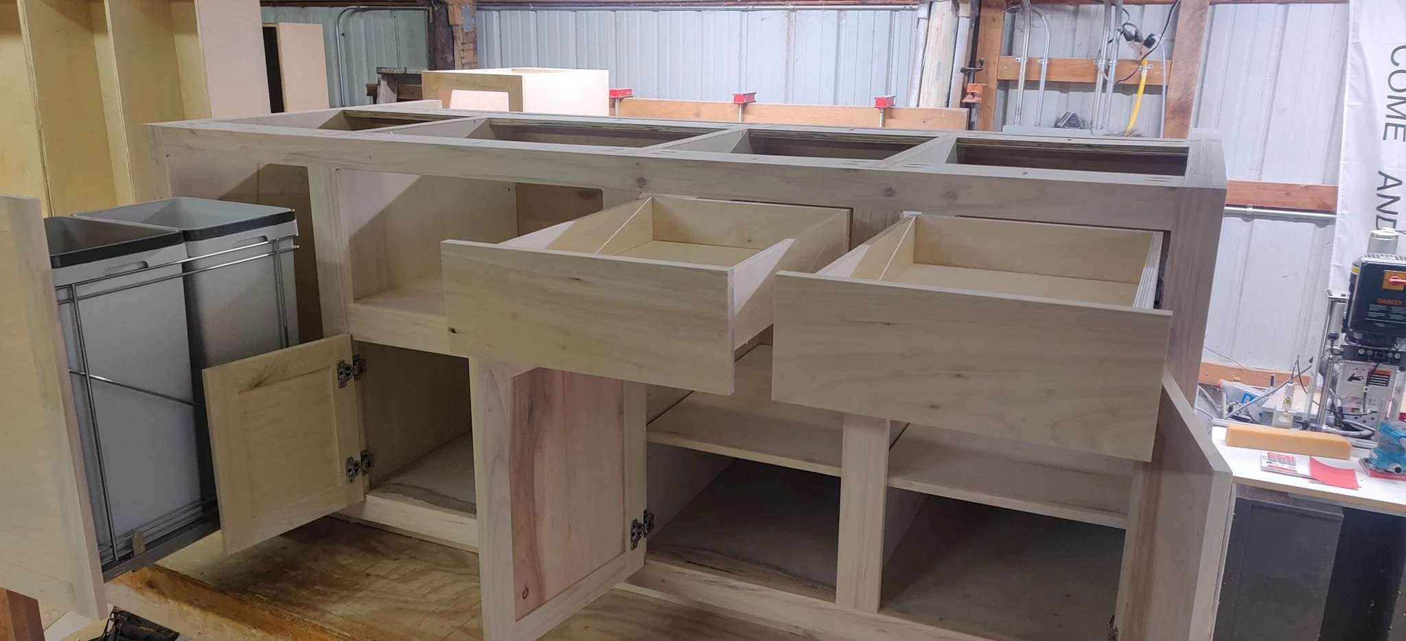 Unfinished wooden cabinet or furniture piece in a workshop, with open storage compartments and doors, partially assembled.