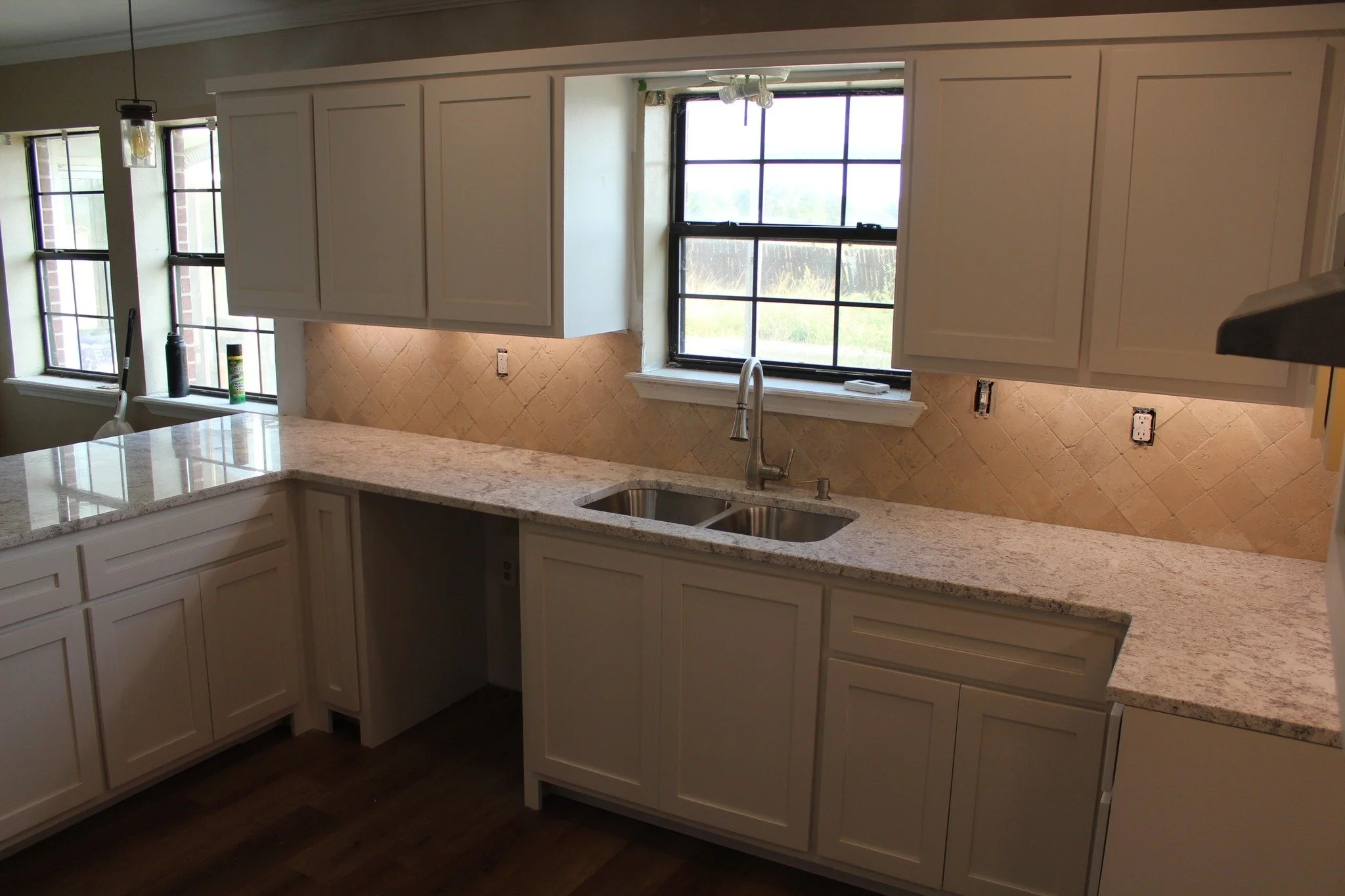 A kitchen with white cabinets, a granite countertop, a double sink, and large windows letting in natural light.