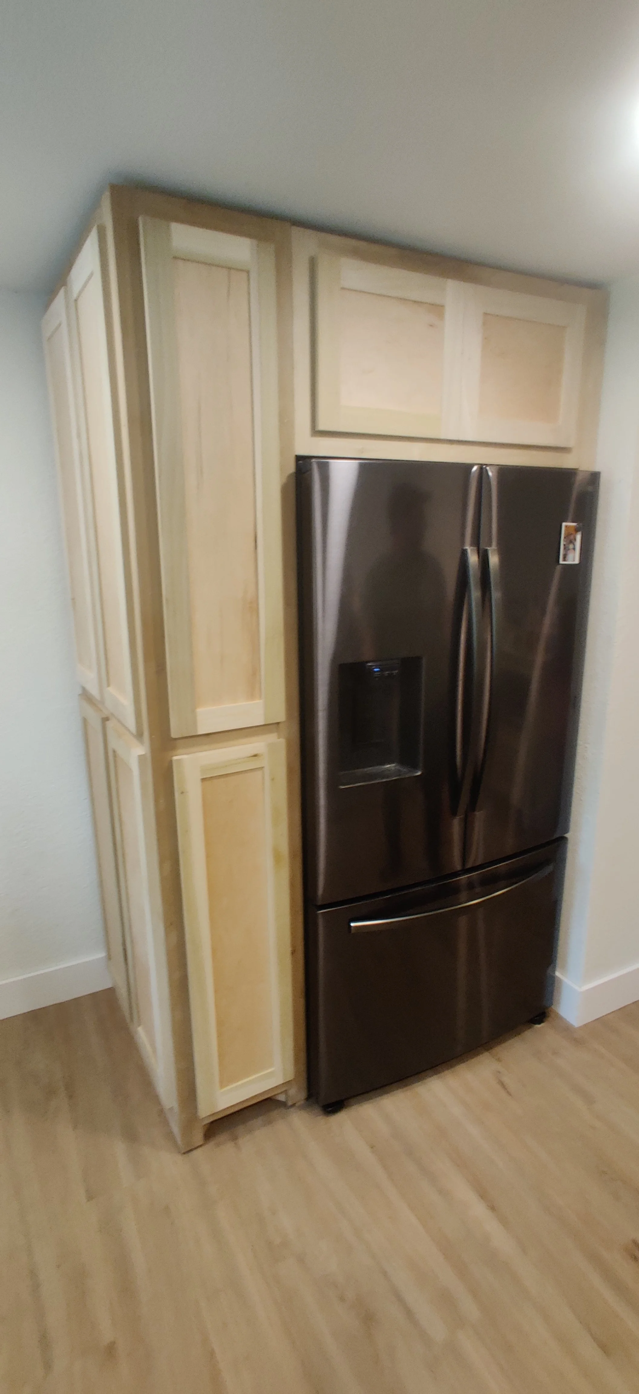 Stainless steel refrigerator next to unfinished wooden cabinets in a kitchen corner.