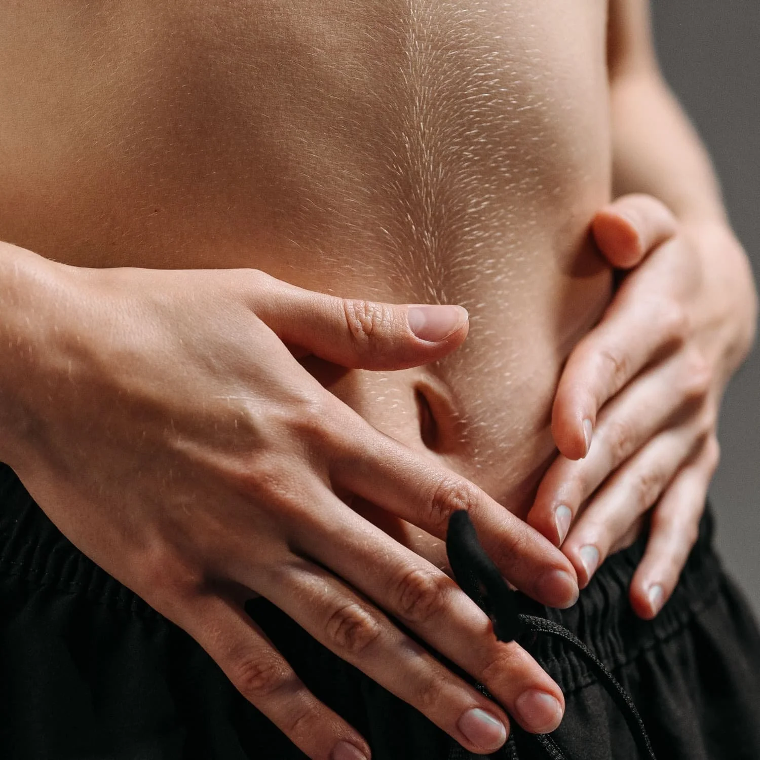 Close-up of a person's stomach being touched by four hands, with a person using a black marker on their stomach.