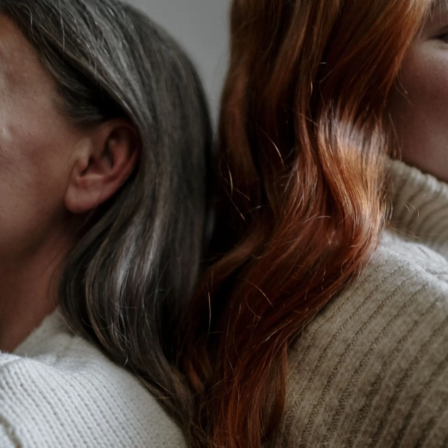 Close-up of two women leaning on each other's shoulders, showing only part of their faces and hair.