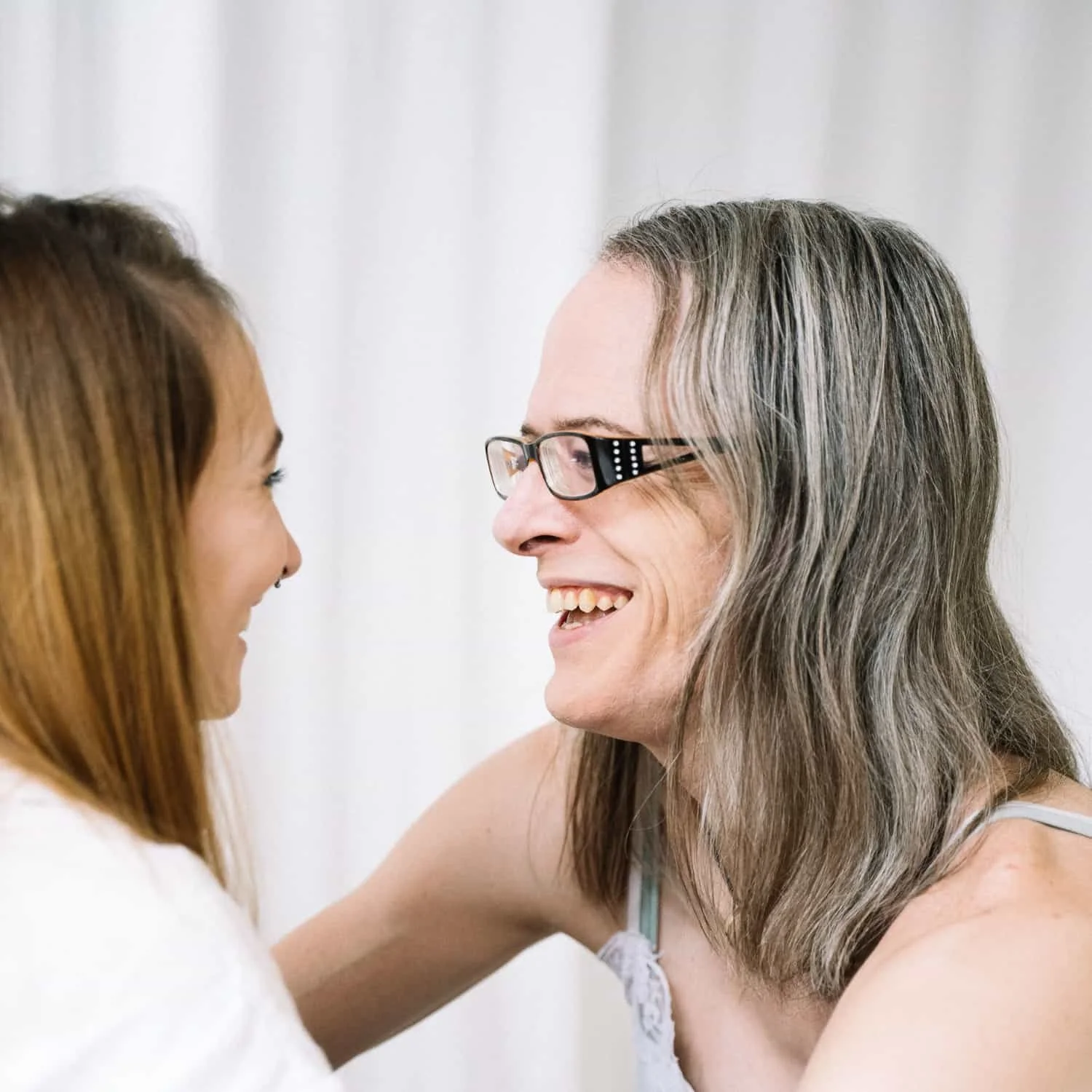 A woman with glasses and long gray hair smiling and talking to a woman with reddish-brown hair and a nose piercing.