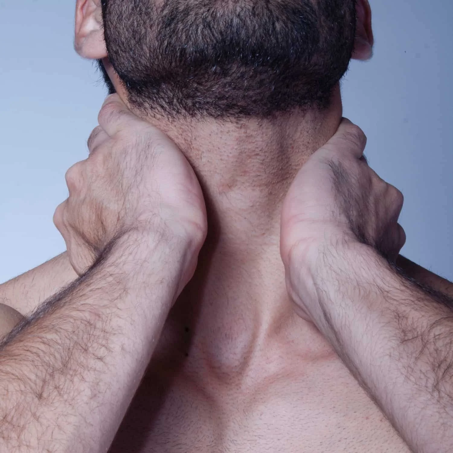 A person with dark hair and skin being massaged or stretched by two other hands on their neck and shoulders, with a light blue background.